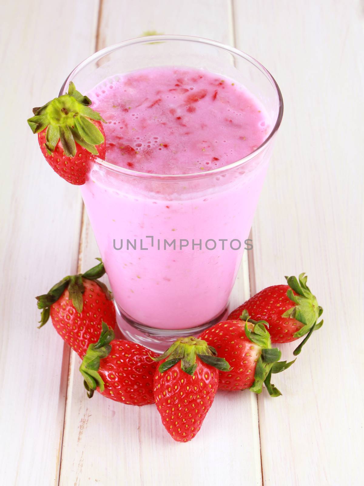 glass of strawberry smoothie on a white wooden background