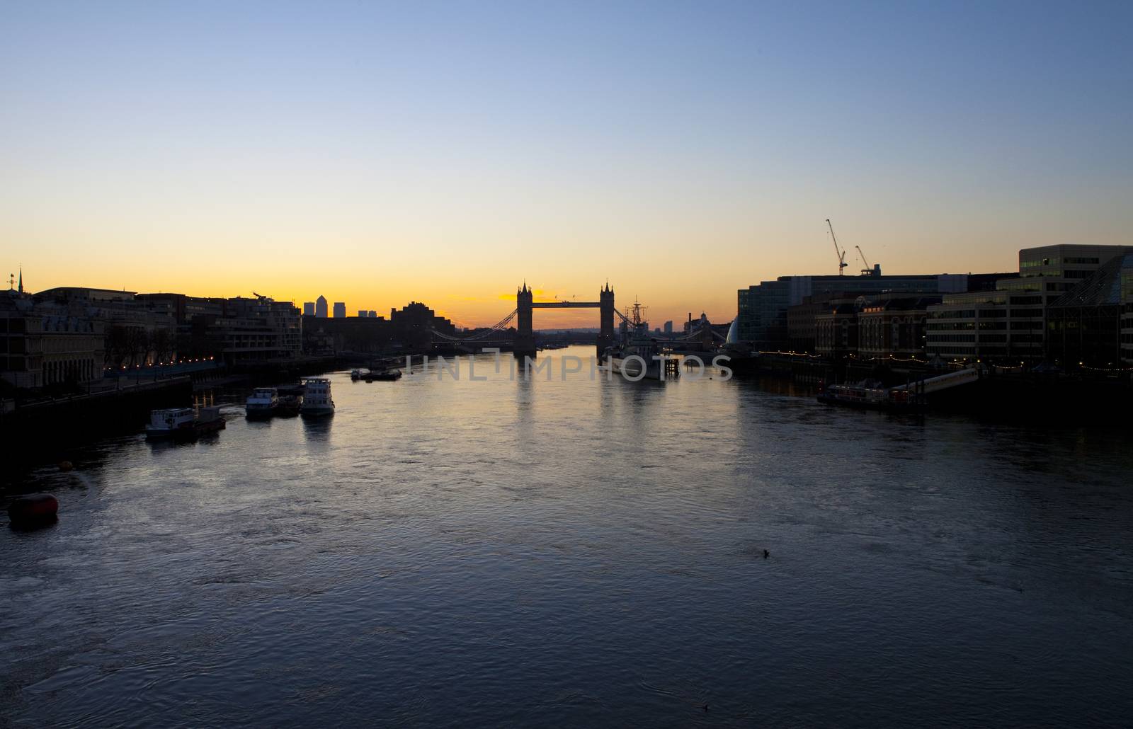 The beautiful sunrise behind Tower Bridge in London.  HMS Belfast, City Hall and the skyscrapers in Docklands are also visible.