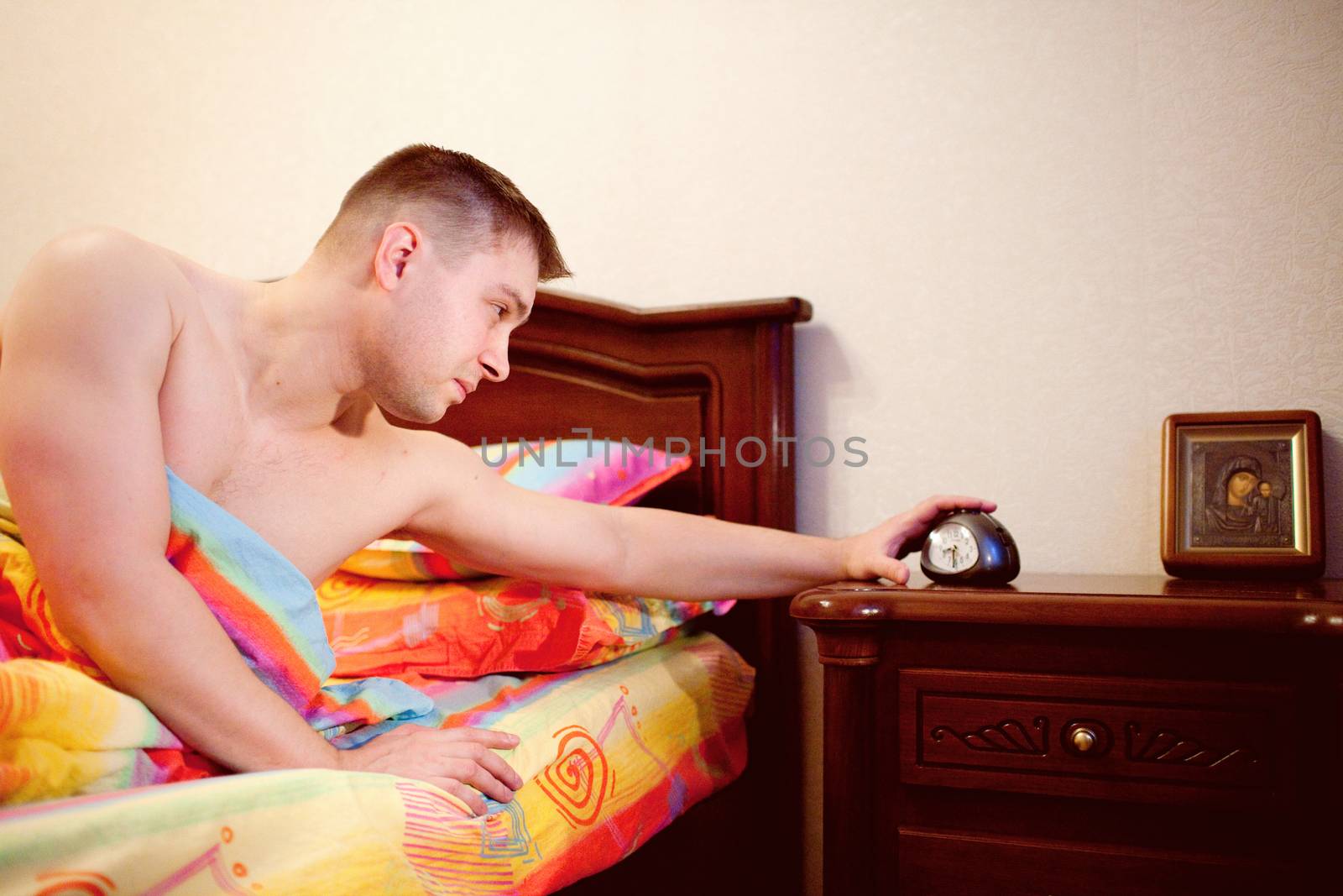 man in bed switching of the alarm clock