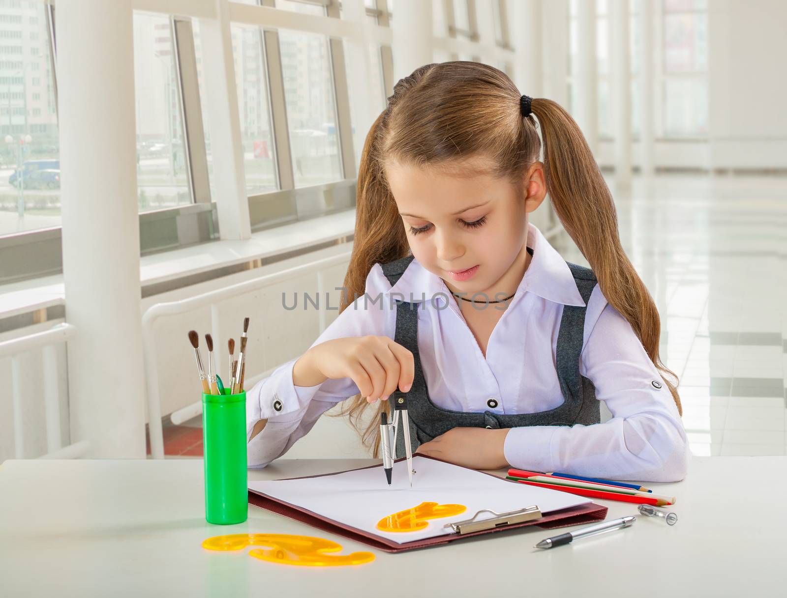 beautiful litle schoolgirl siiting at table and drawing with compass