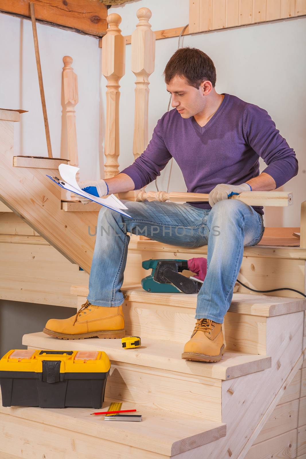 young worker sitting on wooden ladder and loking in blueprint by mihalec