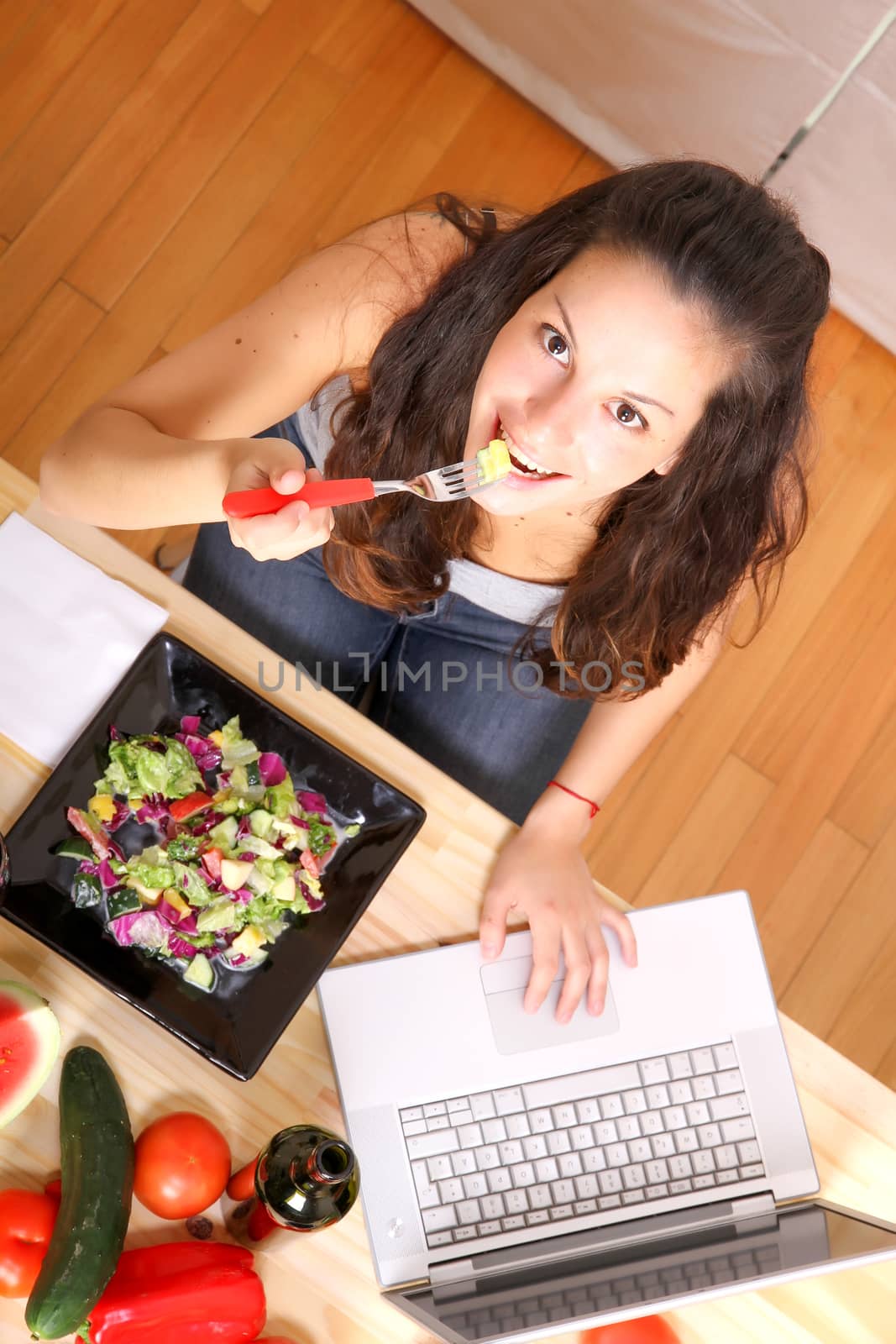 Online information for vegetarians. A young girl eating salad while using a Laptop.