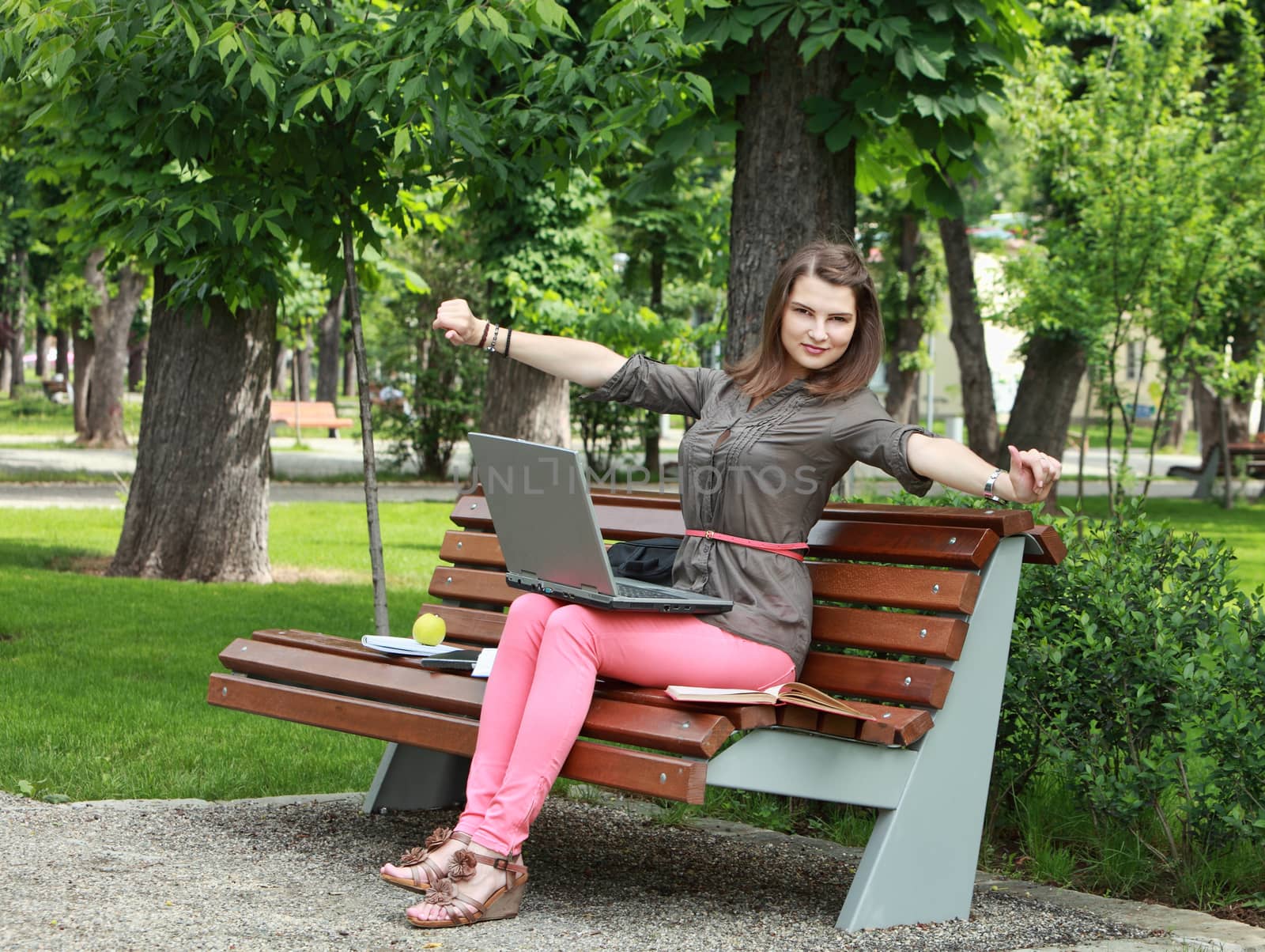 Young woman sitting on a bench in a park with a laptop during a short break of her work.