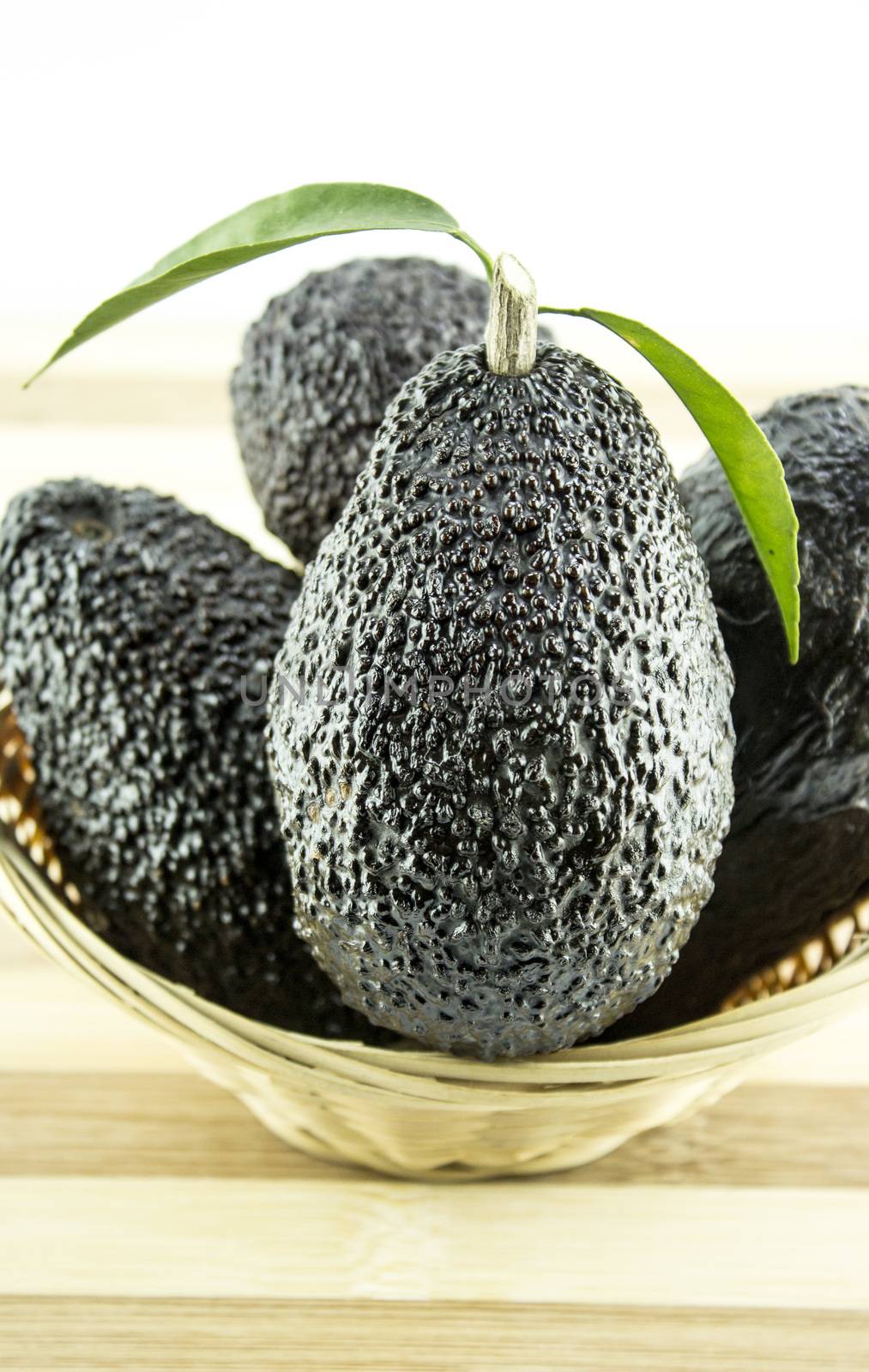 Avocados with leaves on a Dish of straw.