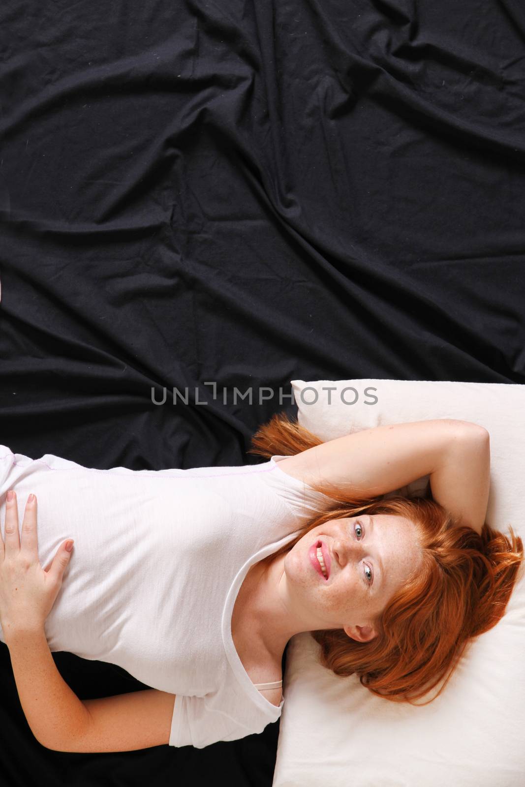 A young adult Woman lying on bed, smiling.
