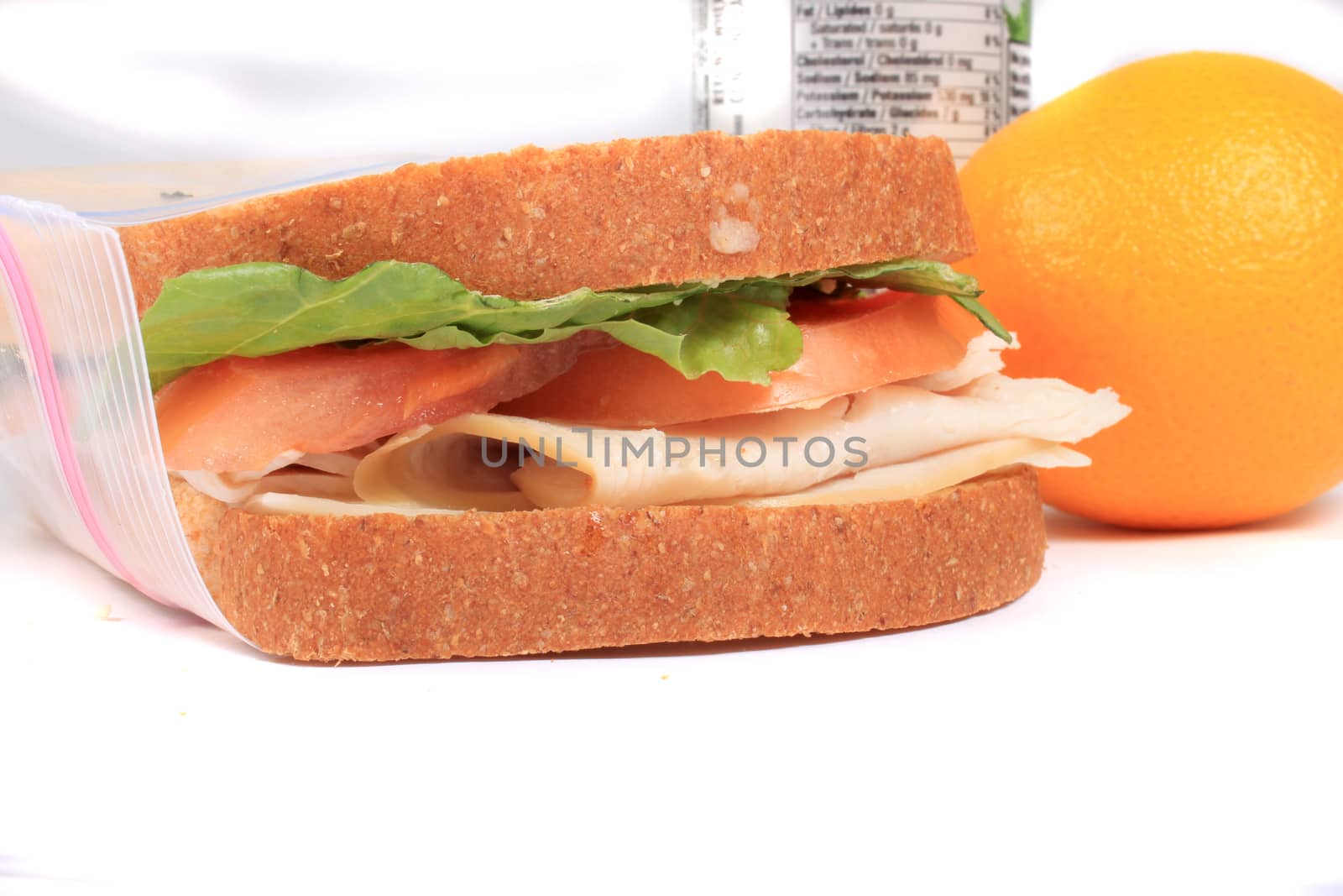 Turkey and cheese sandwich on whole wheat bread with tomato and lettuce inside a zipped bag ready for lunch and orange on the side