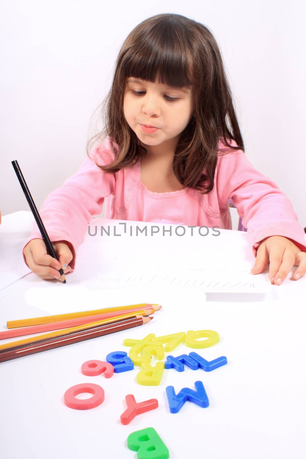 Cute little preschool girl playing with letters and drawing with pencils on white 