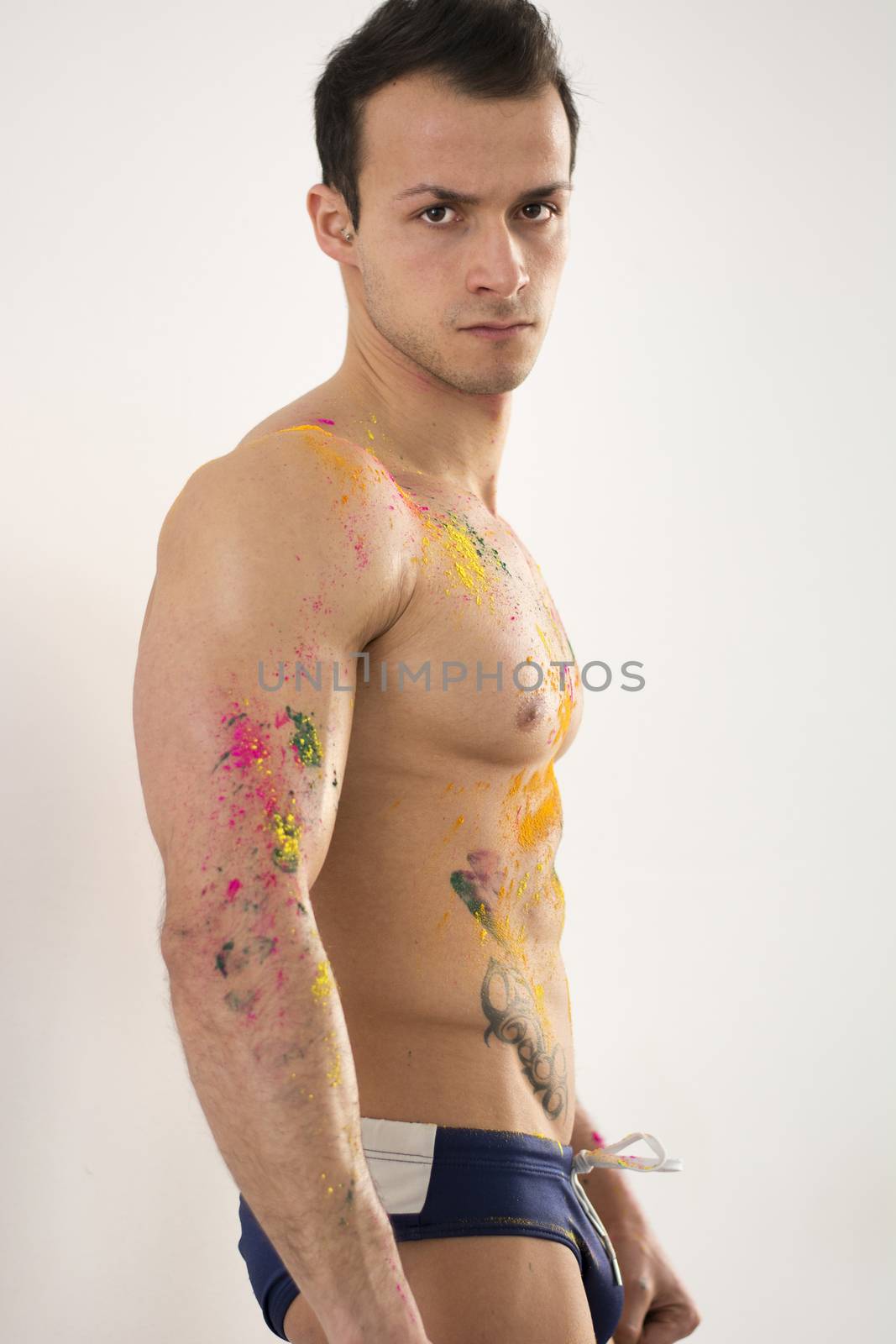 Muscular young man shirtless with skin painted with Holi colors, looking at camera