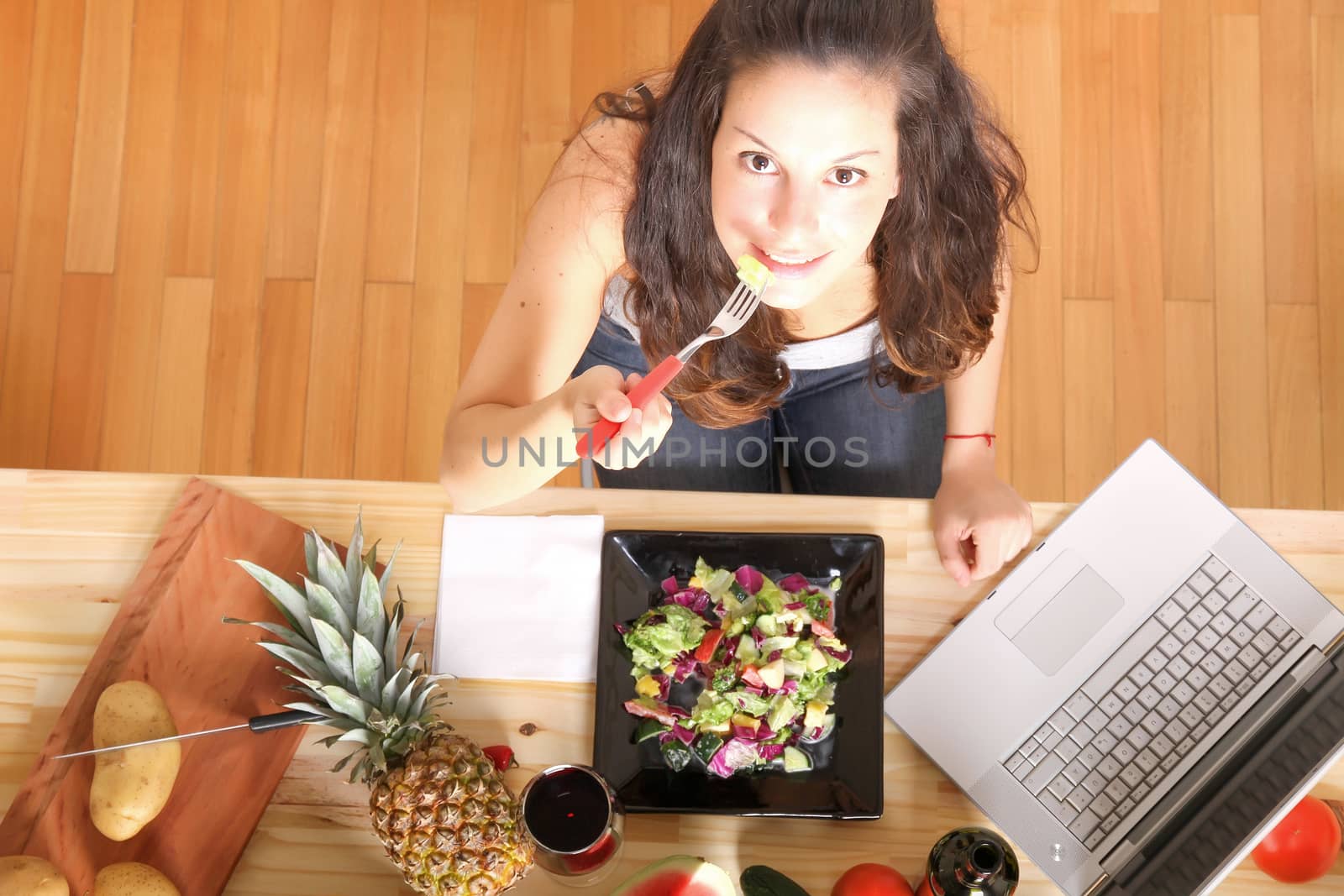 Online information for vegetarians. A young girl eating salad while using a Laptop.