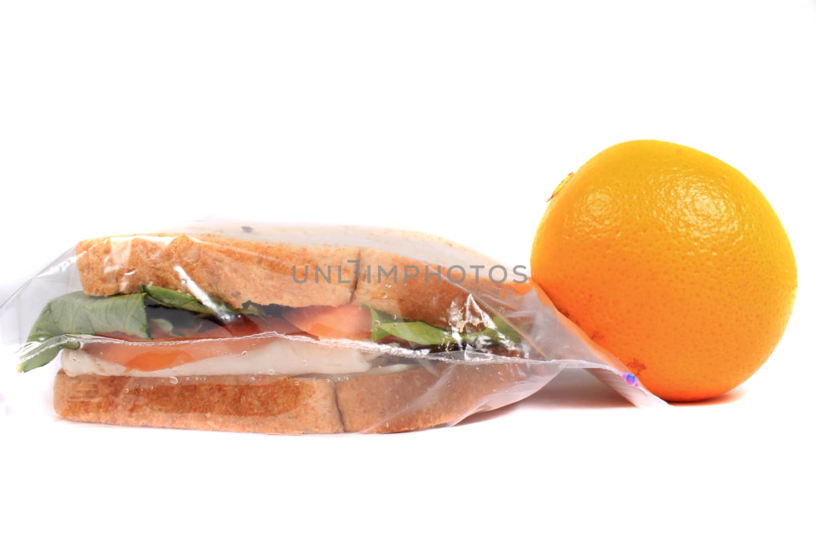 Turkey and cheese sandwich on whole wheat bread with tomato and lettuce inside a zipped bag ready for lunch and orange on the side