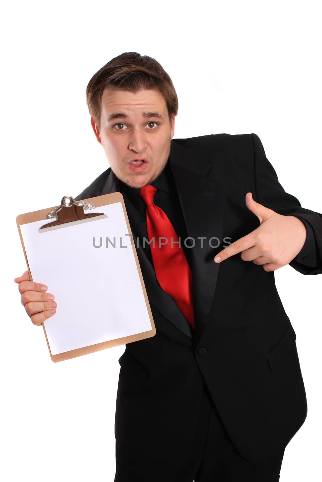 Businessman with funny expression pointing at and holding a clipboard with a blank page on a white background