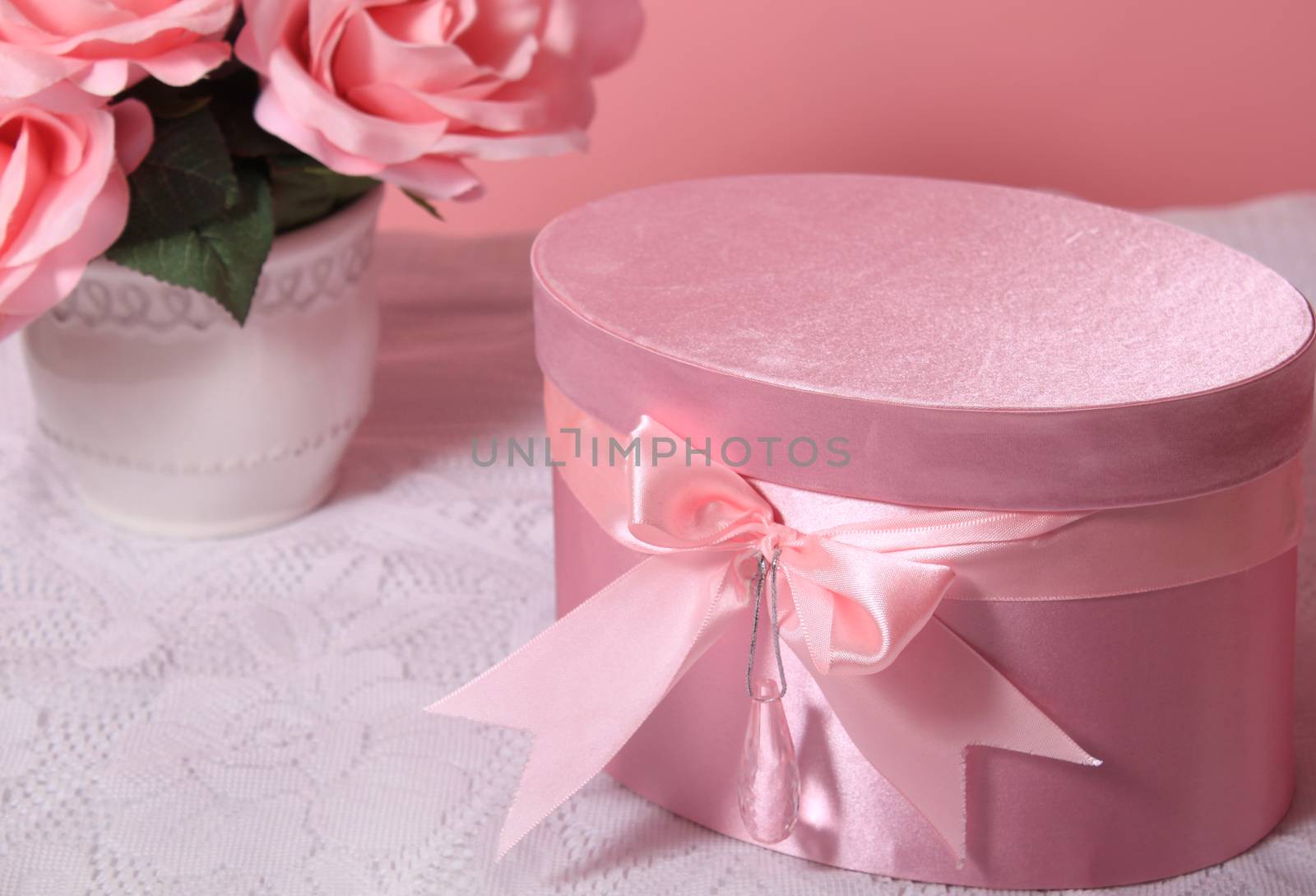 Pretty satin pink bow on box with hanging crystal creating a light reflection and roses in the background