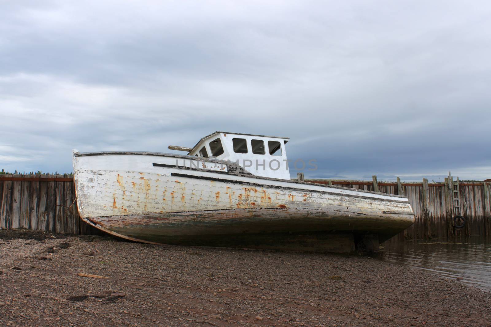 Beached fishing boat leaning against a wooden pier in the Bay of Fund,  Maces Bay, New Brunswick, Canada