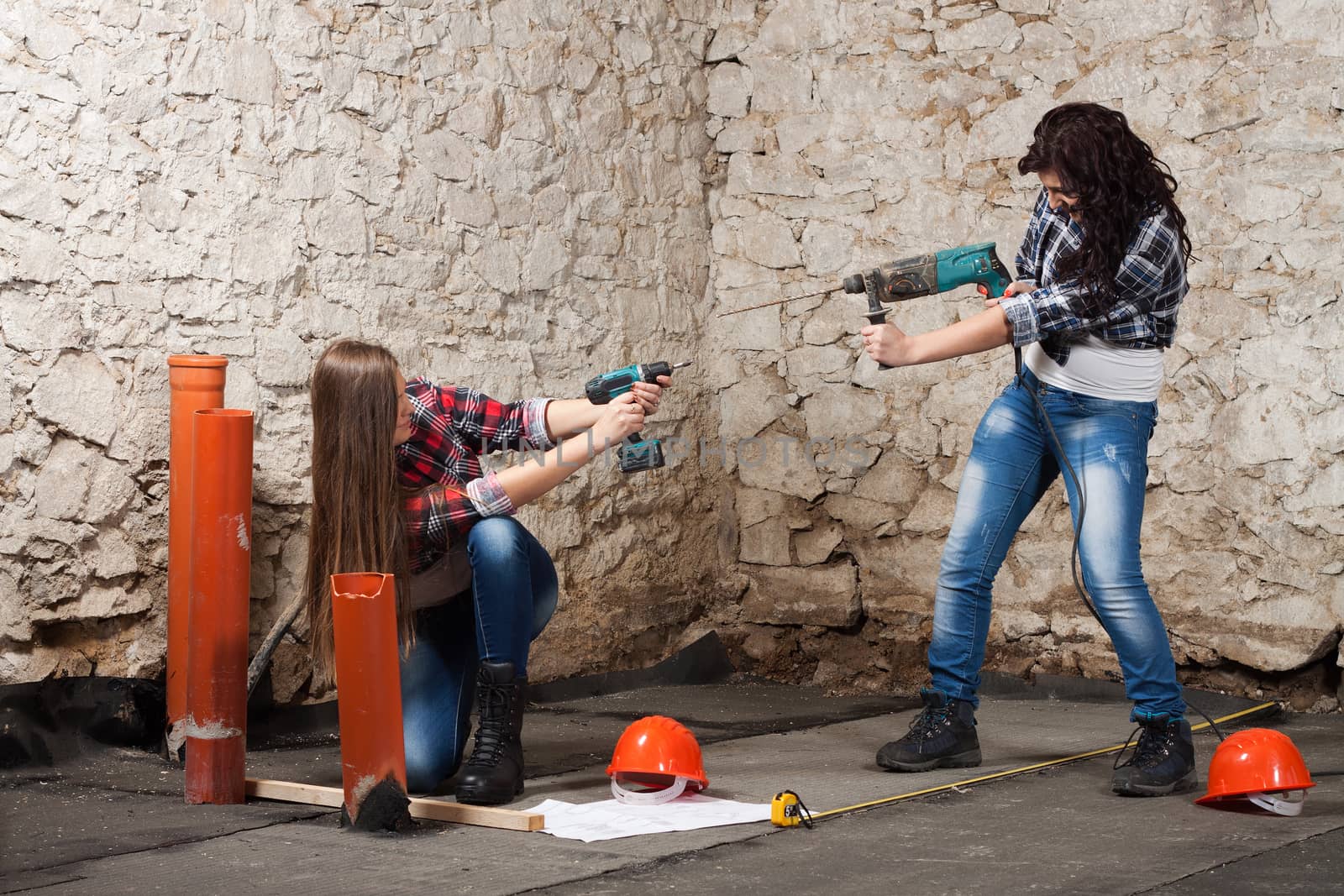 Two young long-haired woman works to repair an old house with an electric drill and cordless screwdriver