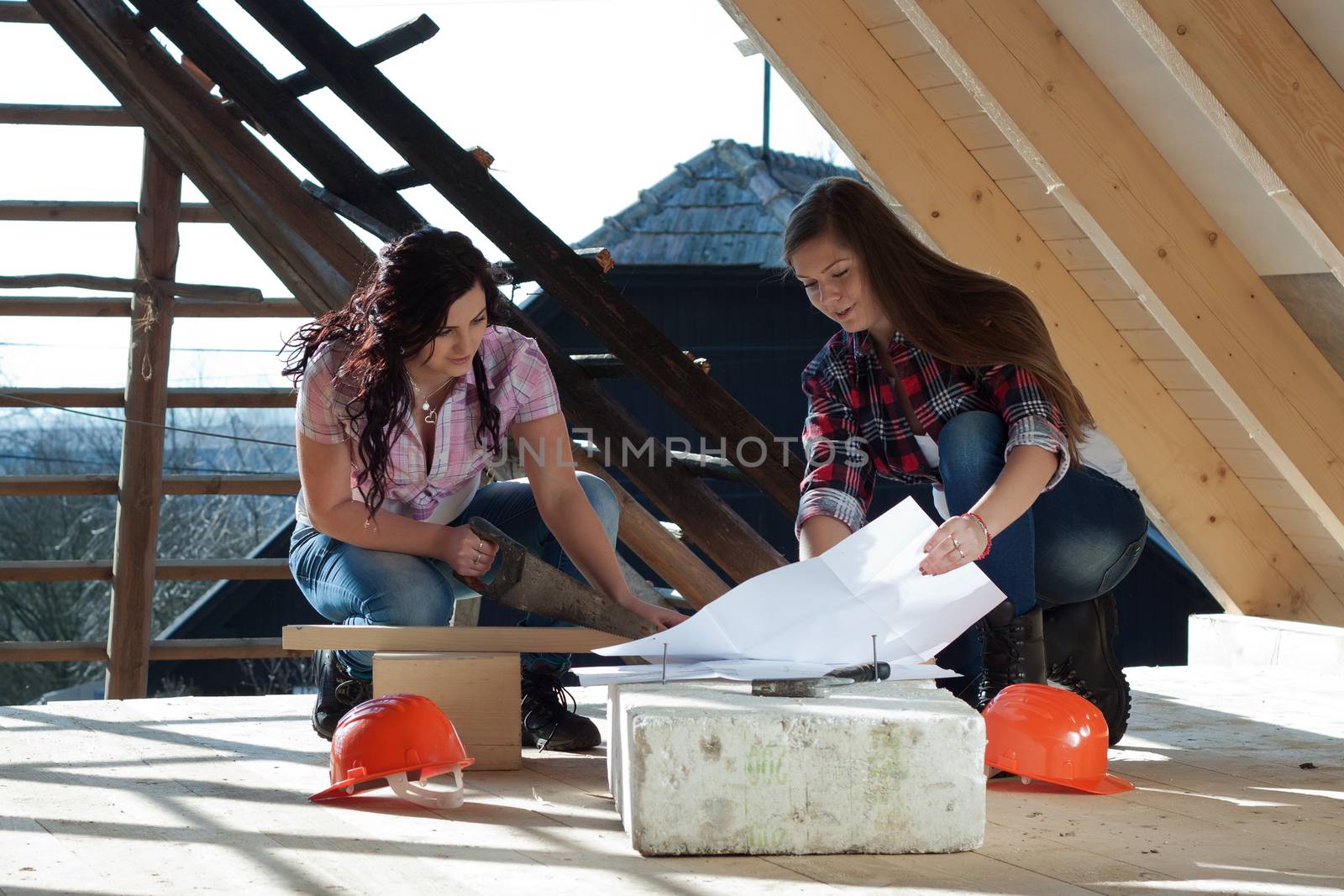 Two young long-haired woman sawed wood for the roof of the house in accordance with drawing