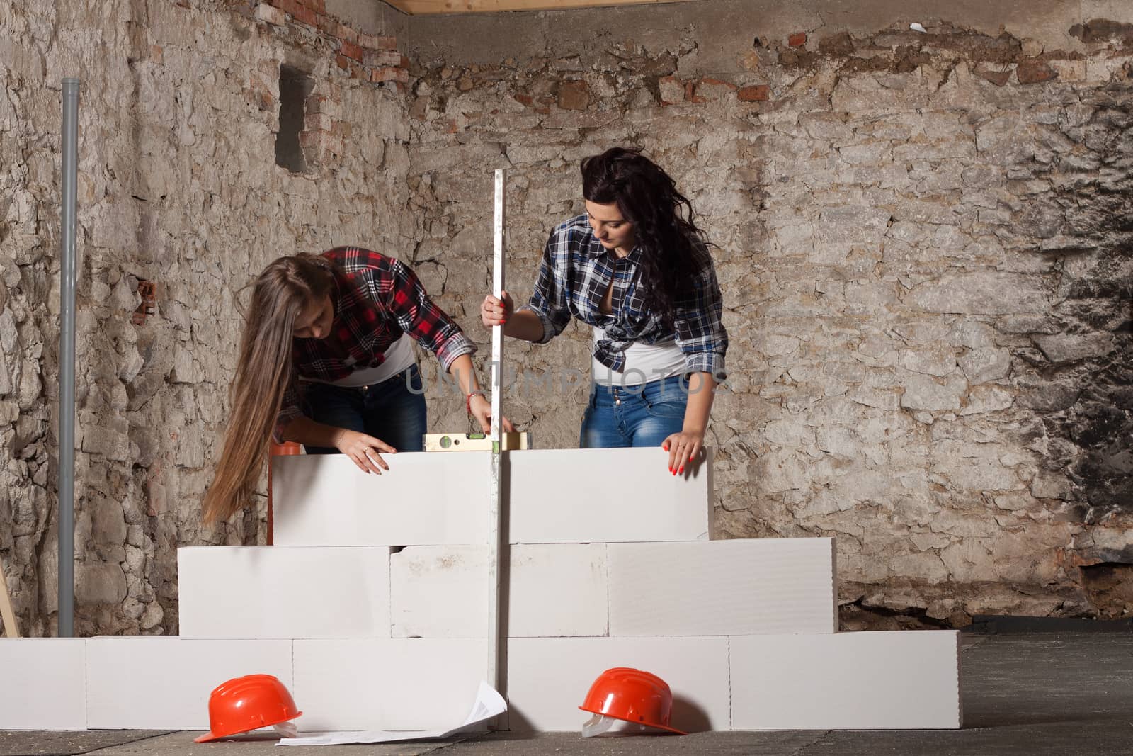 Two young long-haired woman repairing the old house and build a new wall from blocks in accordance with drawing