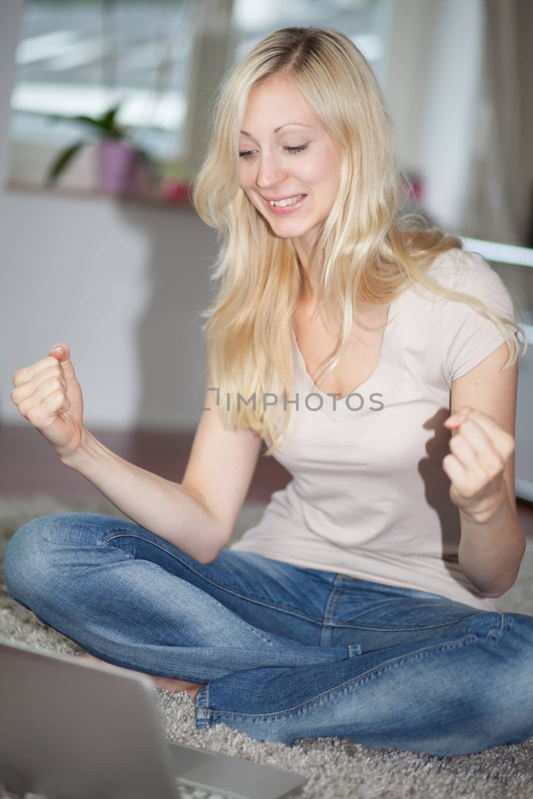 Blonde girl rejoicing while is using a laptop computer