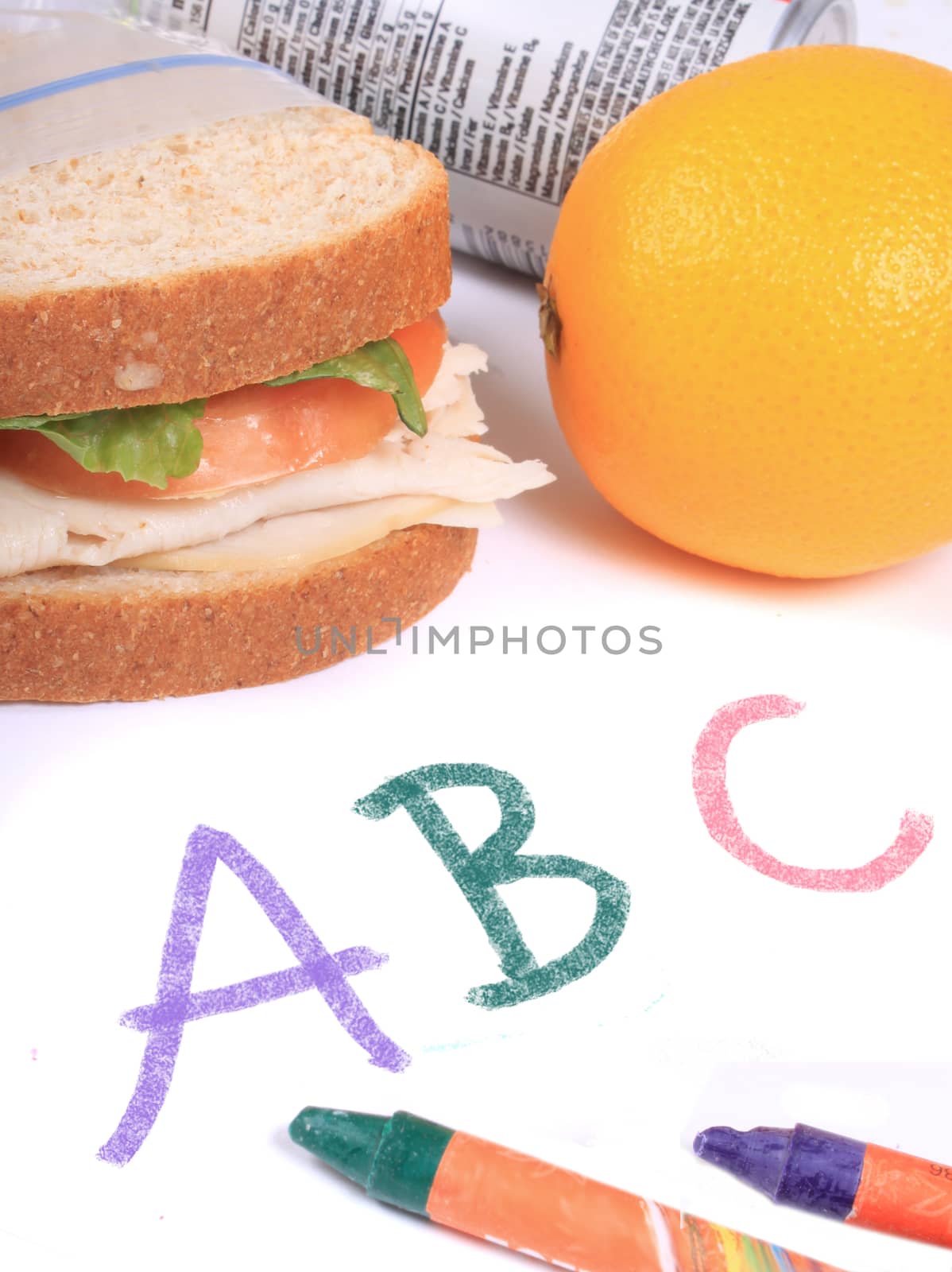 Turkey and cheese sandwich on whole wheat bread with tomato and lettuce inside a zipped bag ready for lunch and orange and juice can on the side on top of abc paper