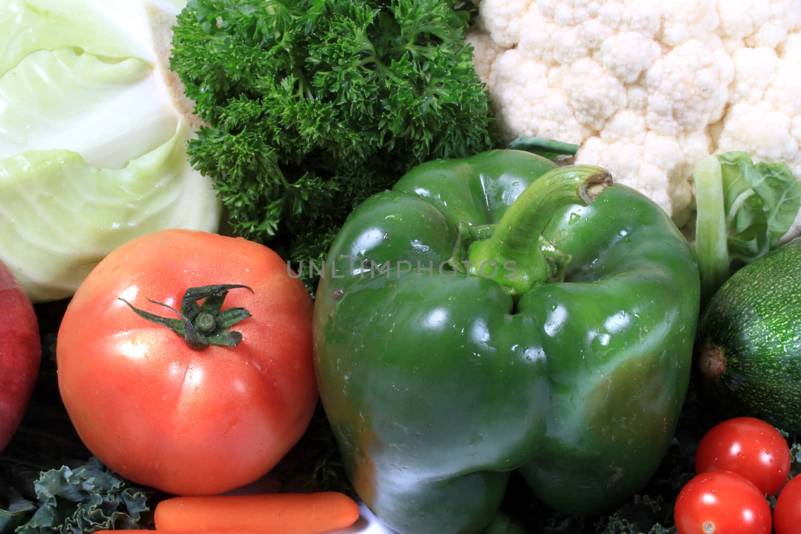 Colorful red  tomato and green pepper surrounded by  vegetables such as cabbage and parsley and cauliflower