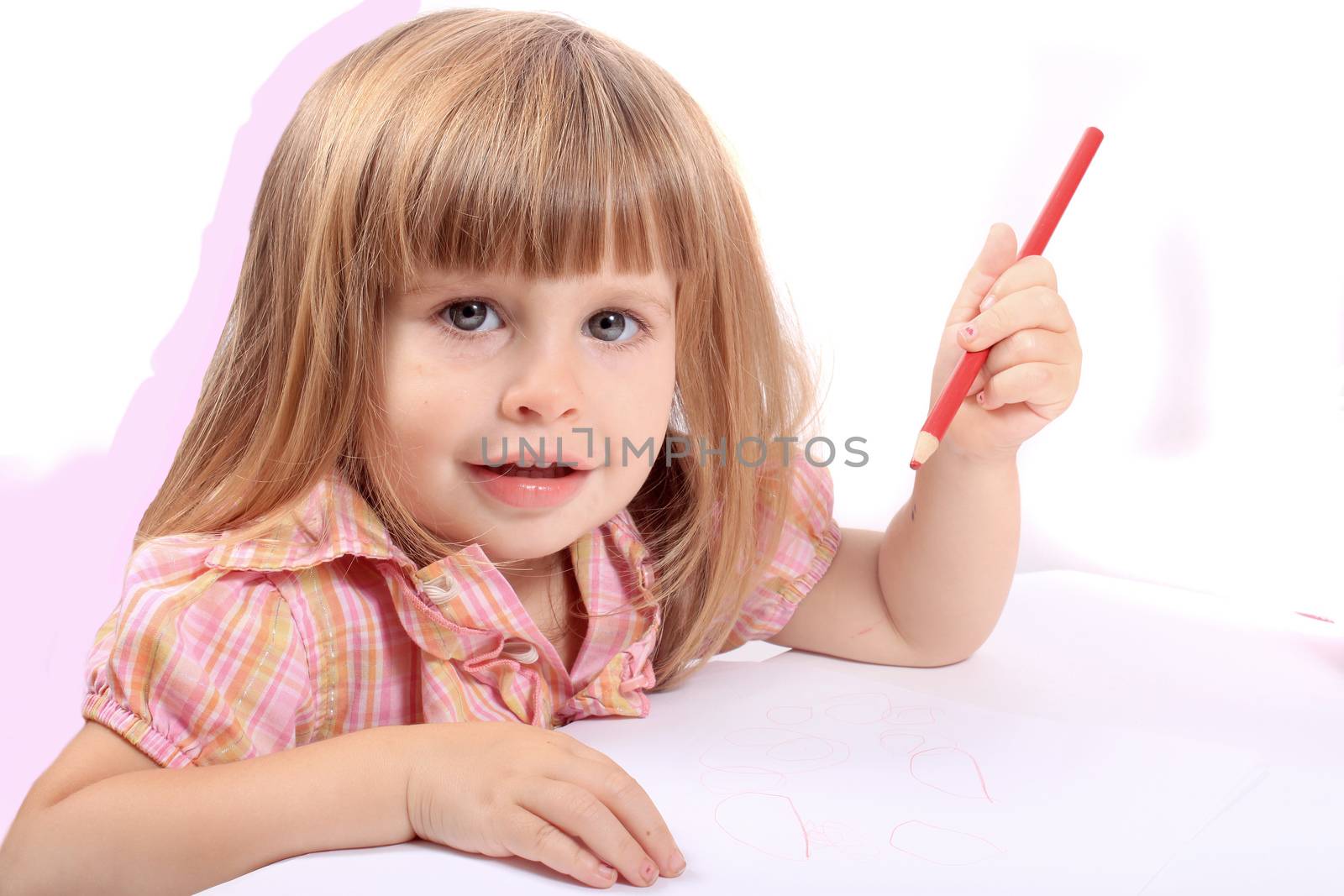 Cute little two year old girl draws pictures on white paper looking and smiling at camera