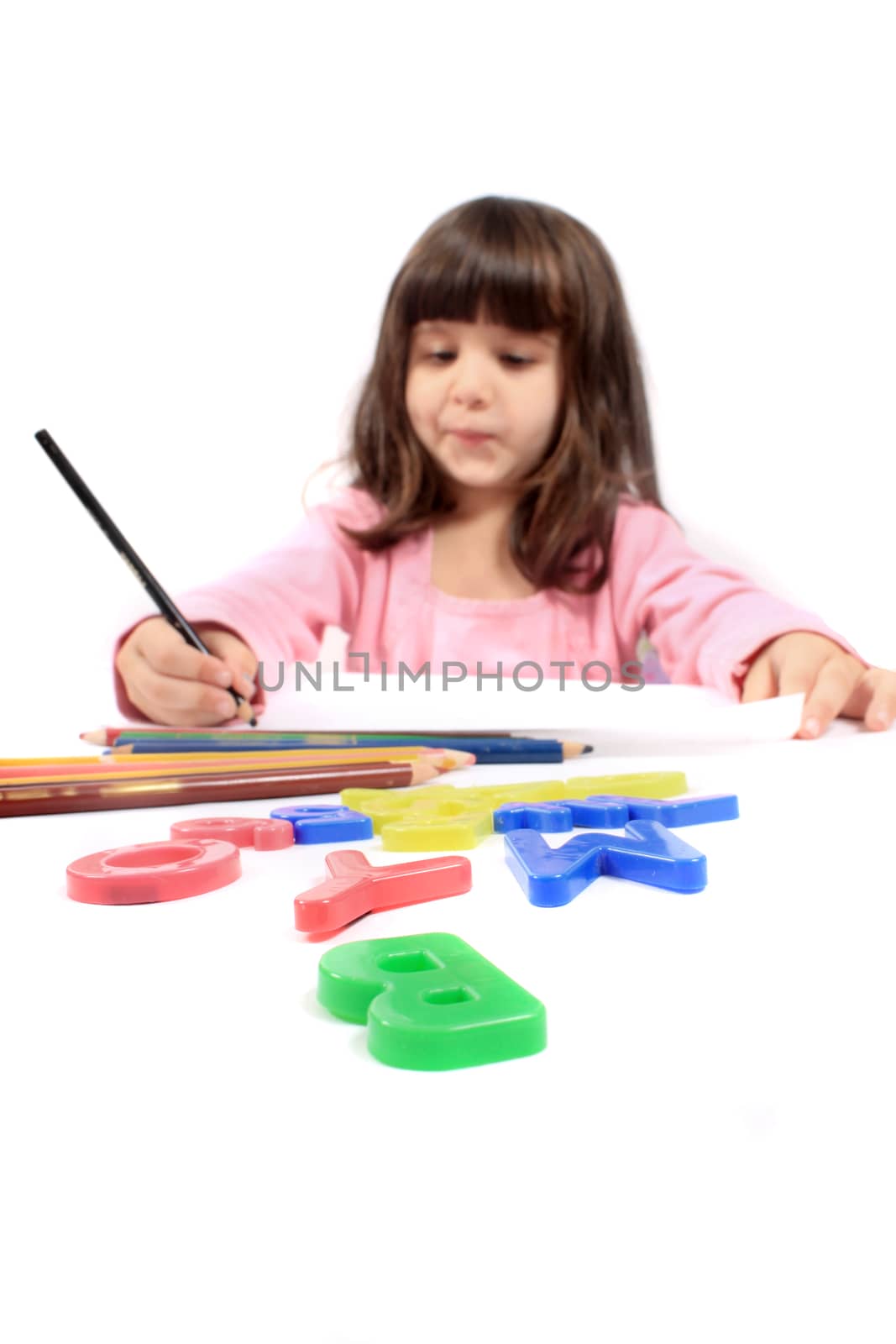 Cute little preschool girl playing with letters and drawing with pencils on white 