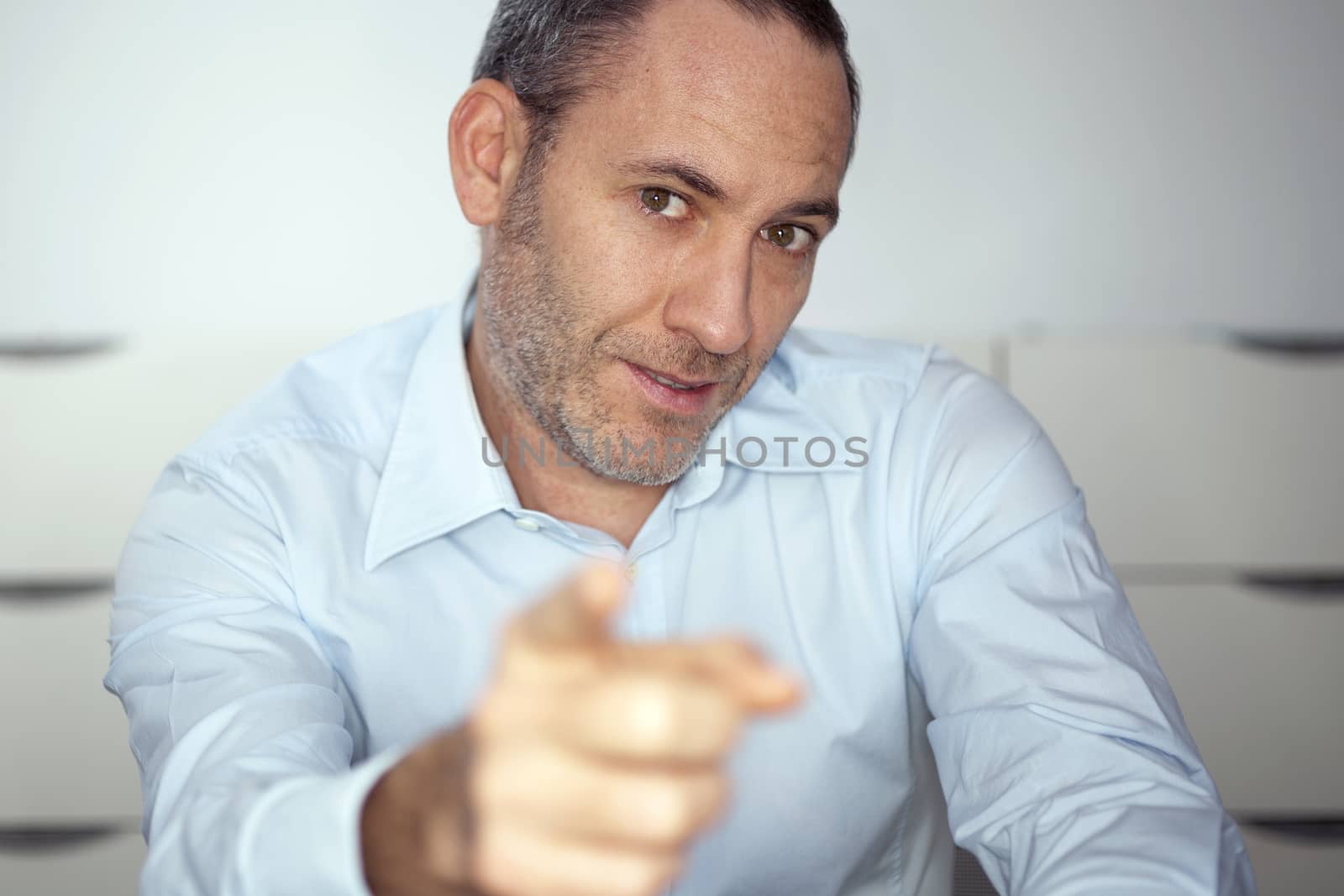 mature well dressed businessman is pointing into the camera