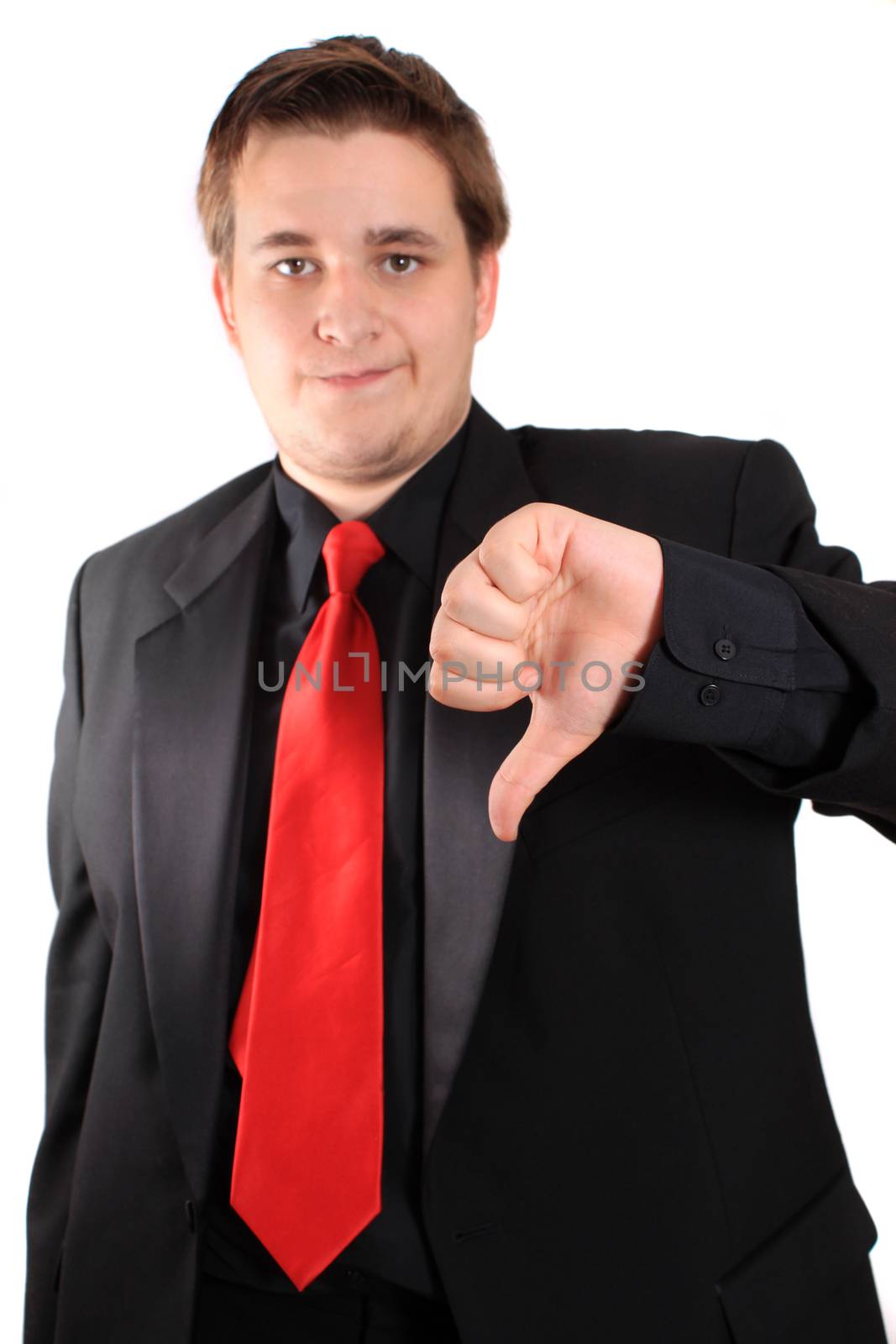 Young handsome businessman in black suit and red tie gives the thumbs down about a situation on a white background