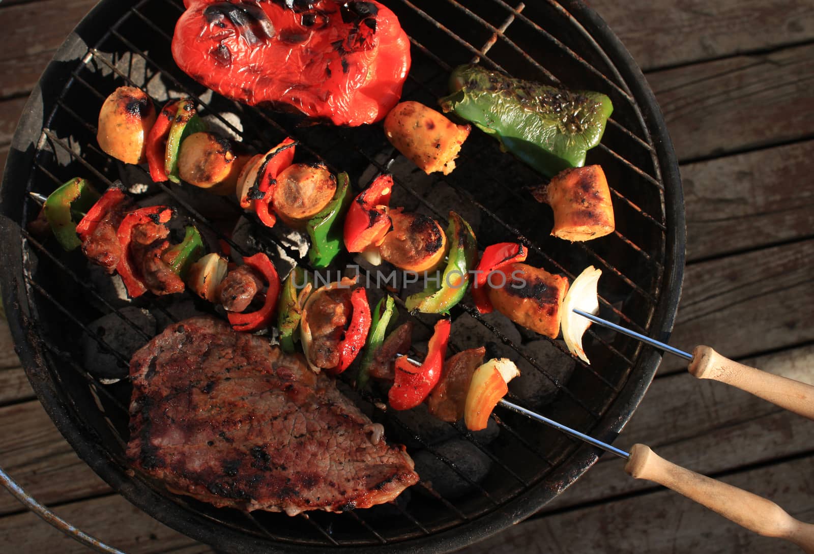 Barbecuing shish kabobs with sausage, steak and peppers, in green and red on a portable charcoal bbq