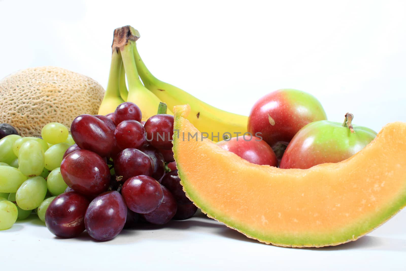 Colorful fresh fruits like grapes, cantaloupe,apples,bananas ,and grapes on a white background