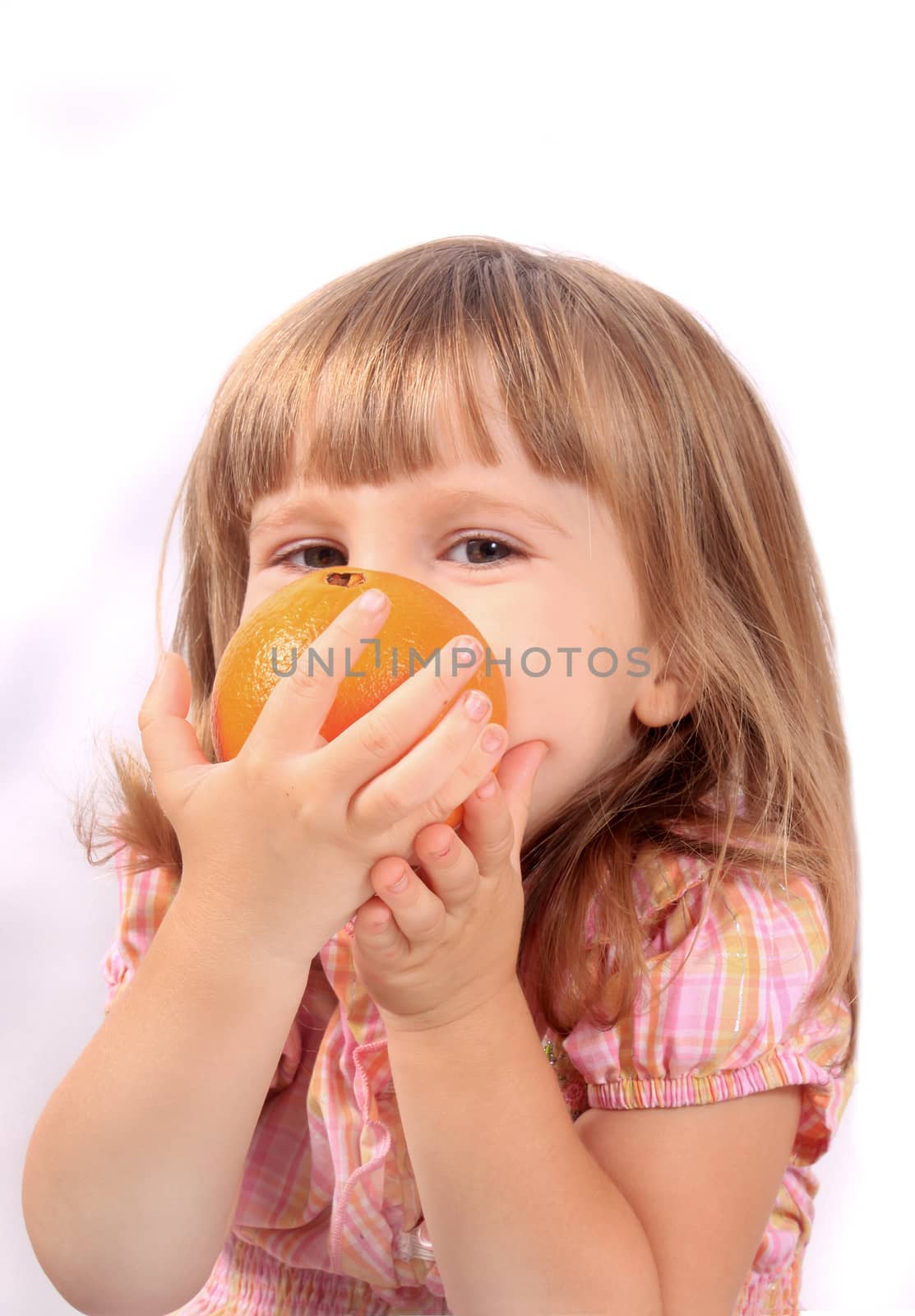 Cute little blonde girl holding and smelling a healthy orange 