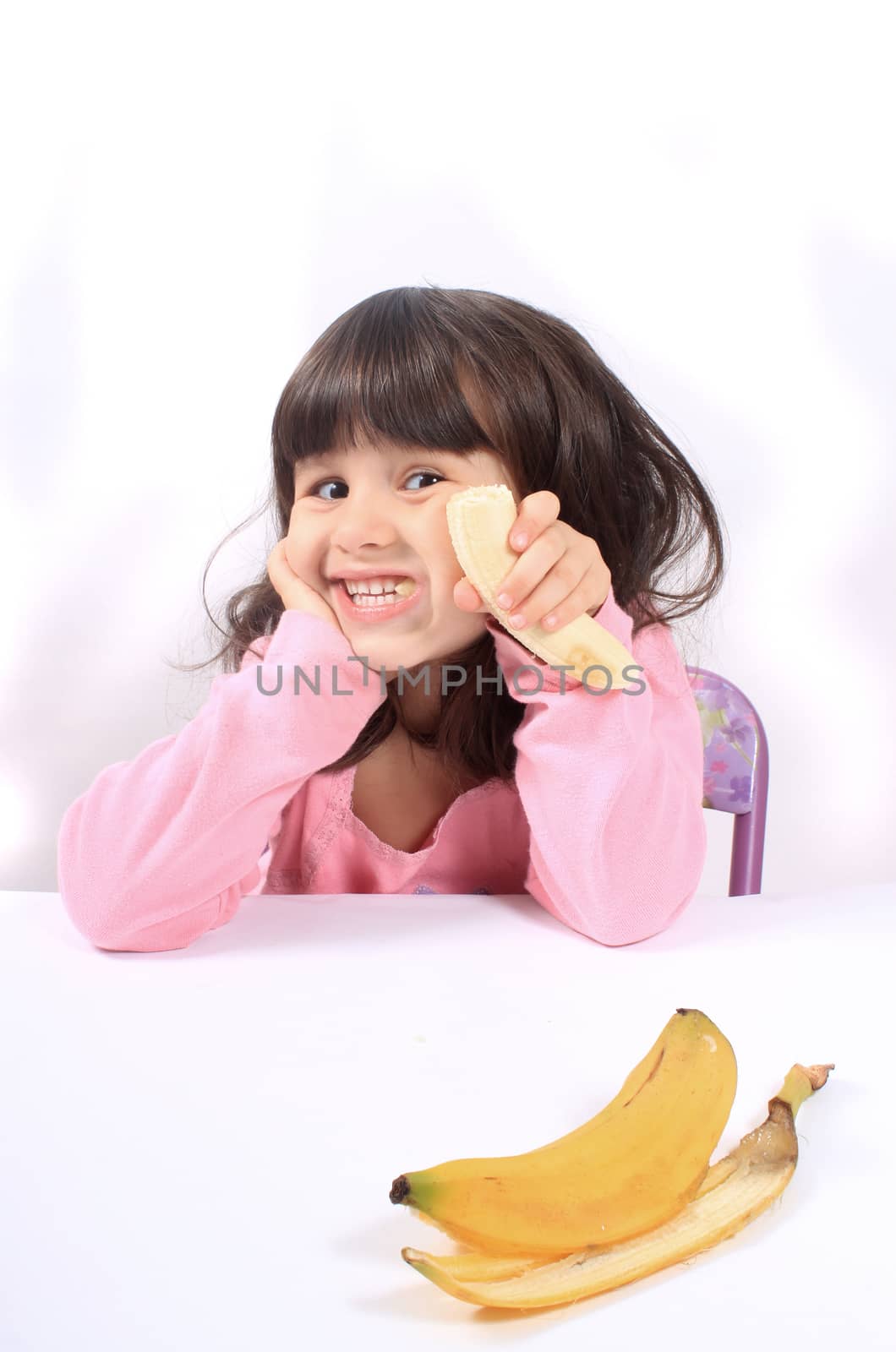 Young little girl making a funny face eating a healthy banana