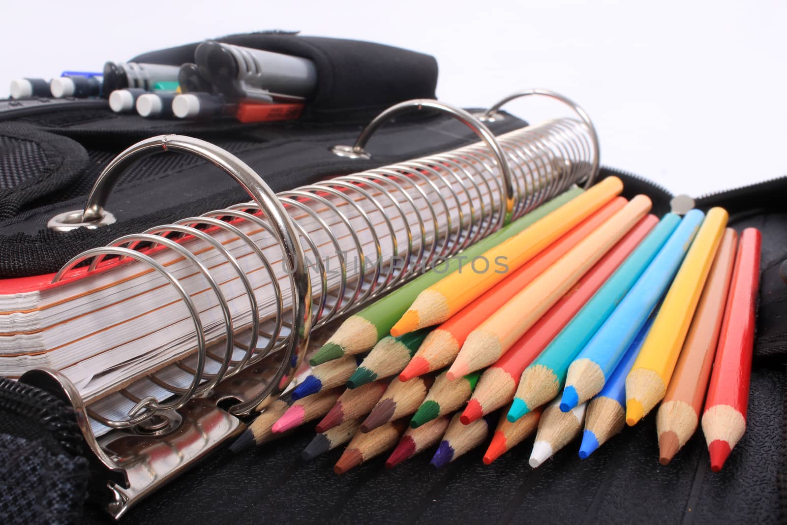 Colorful sharpened  pencil crayons for school  beside  three ring binder containing pens and pencils in pocket