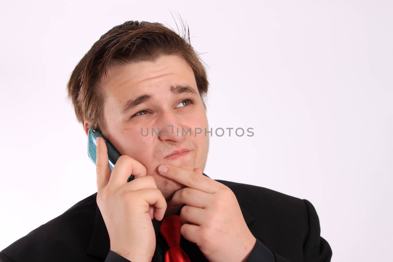 Handsome young businessman in black formal suit with red tie with unsure look on his face while talking on cellphone