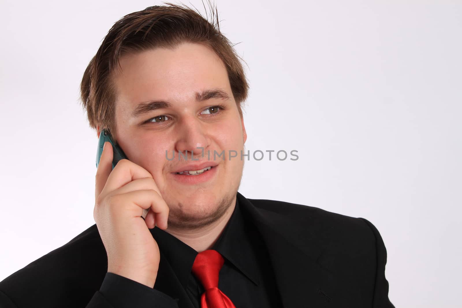 Handsome young businessman in black formal suit with red tie talking and smiling on cellphone