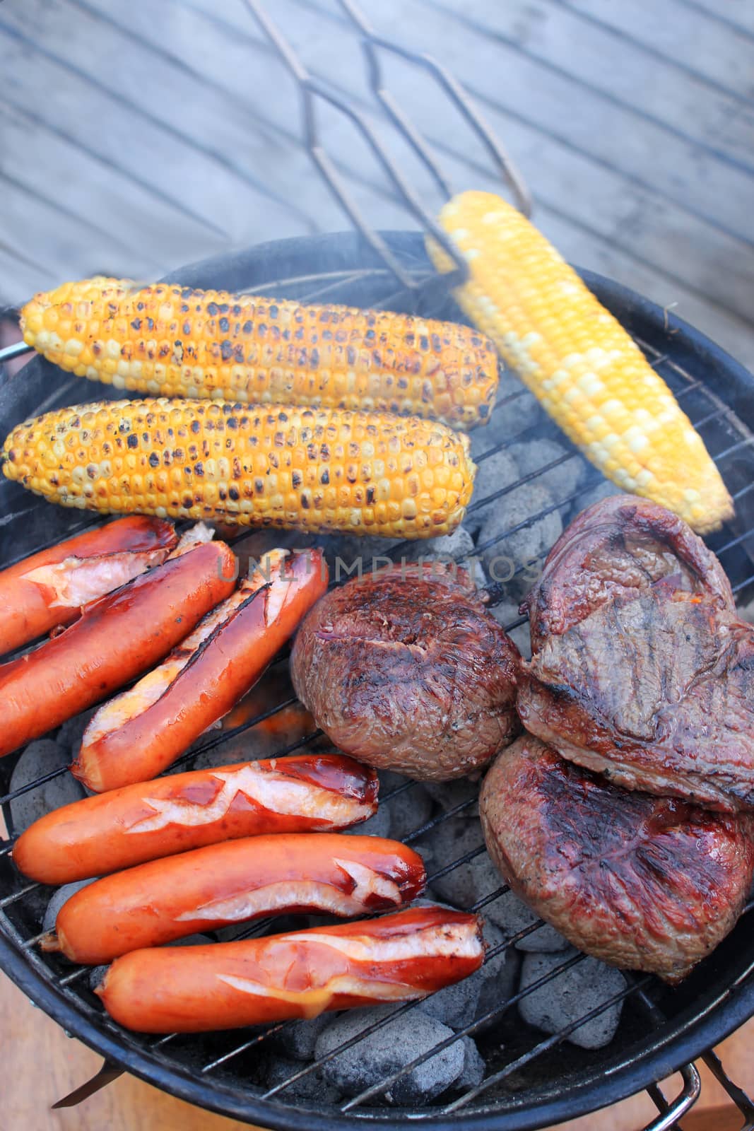 Smokey barbecue cooking on coals in the great outdoors consising of corn on the cob, round steak, and sausages