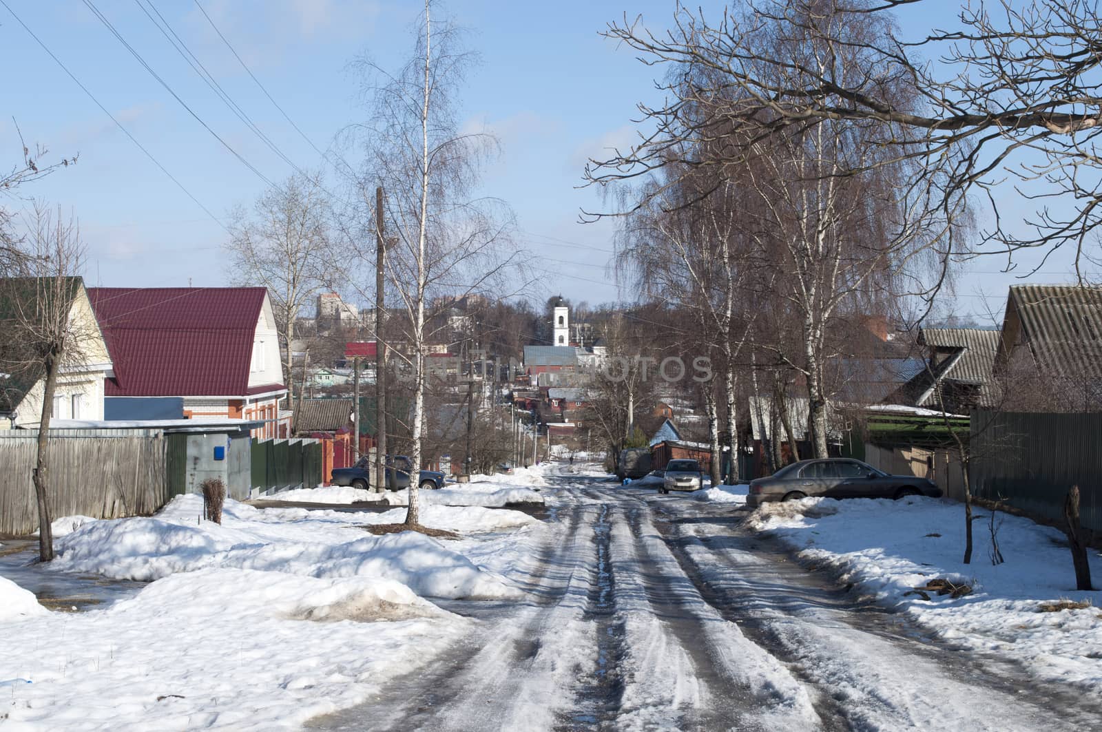 Road with melting snow in a small provincial town on sunny spring day