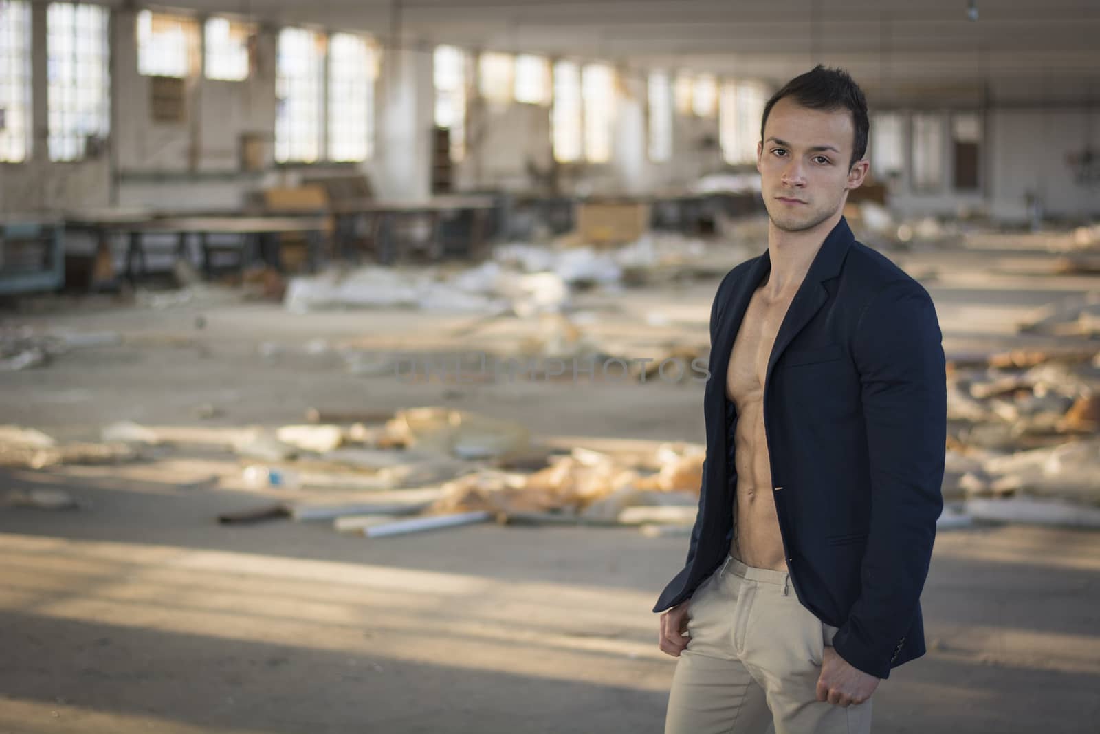 Muscular young man with jacket on naked torso in empty abandoned workplace
