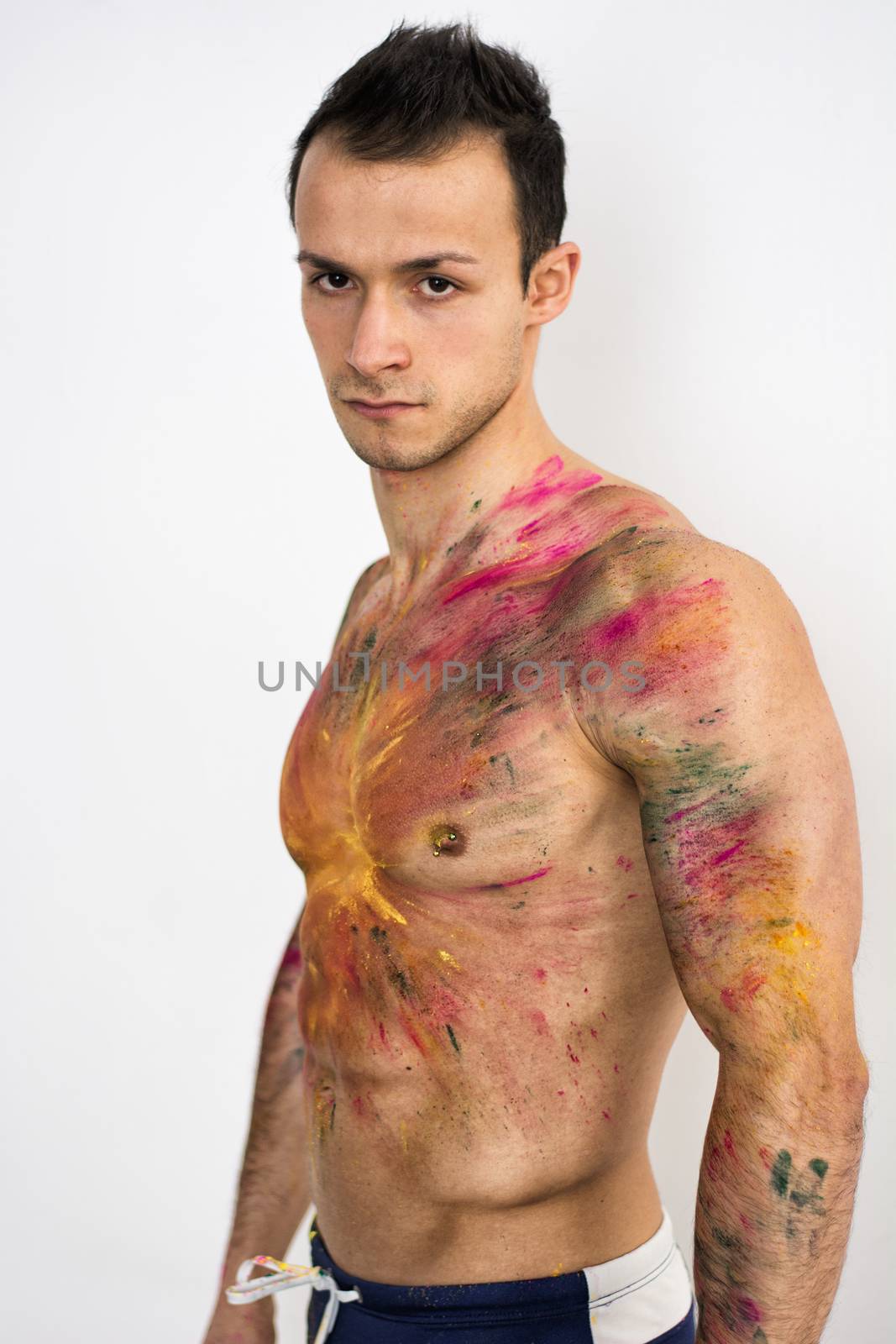 Muscular young man shirtless with skin painted with Holi colors, looking at camera