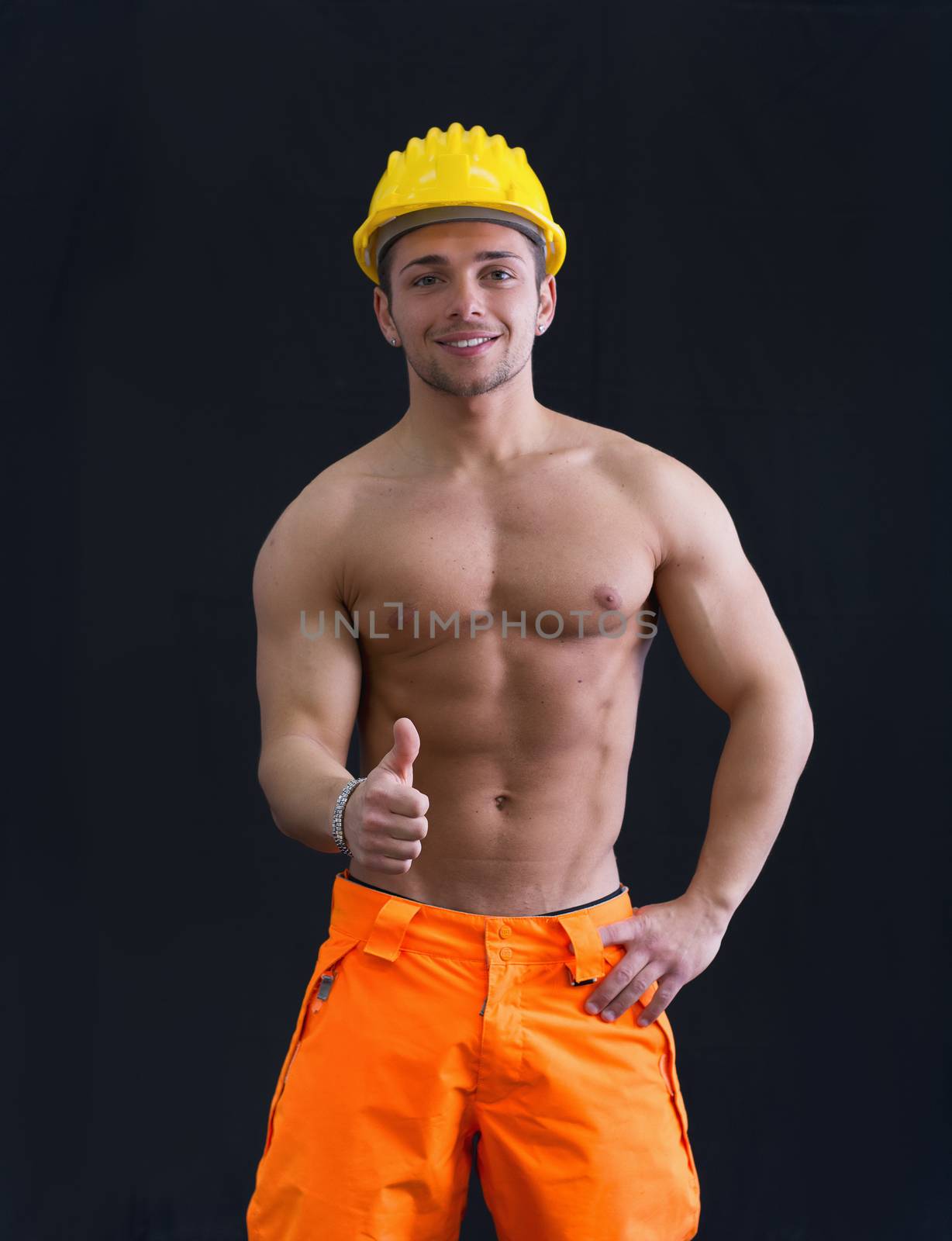 Muscular young construction worker shirtless wearing hardhat doing thumb up sign for OK