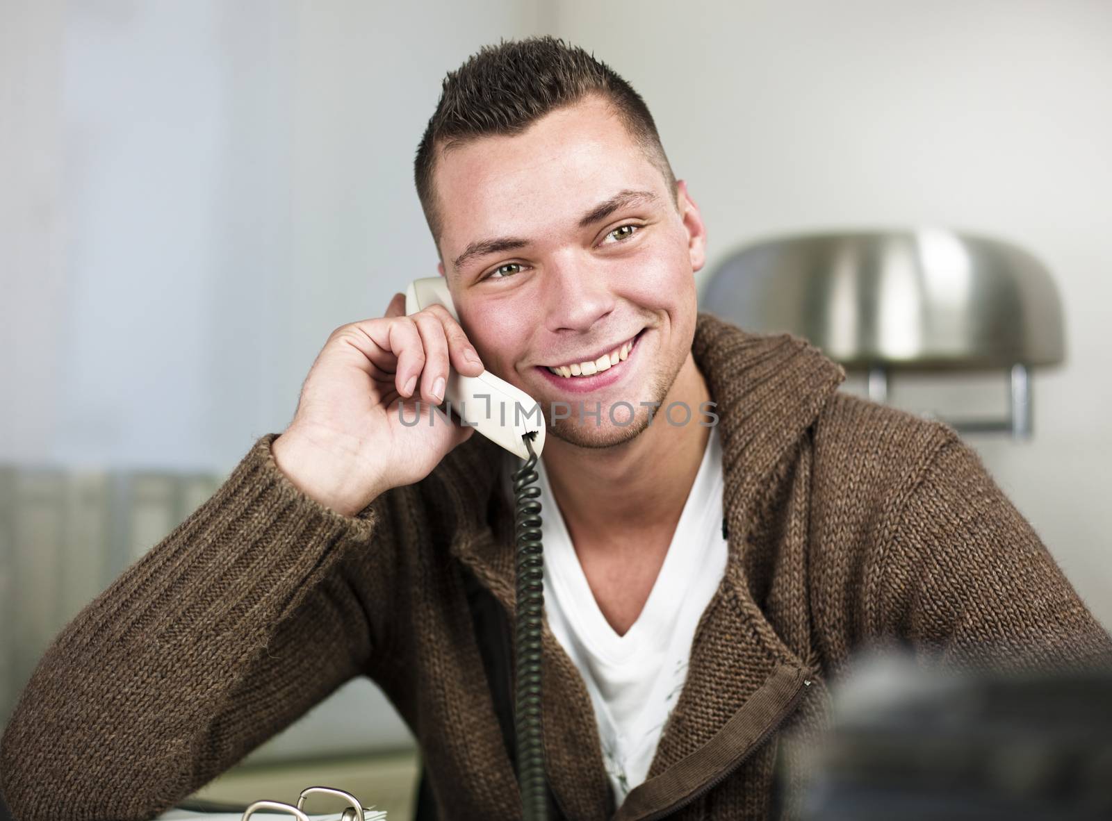 Smiling young businessman having conversation on landline phone. Horizontal shot