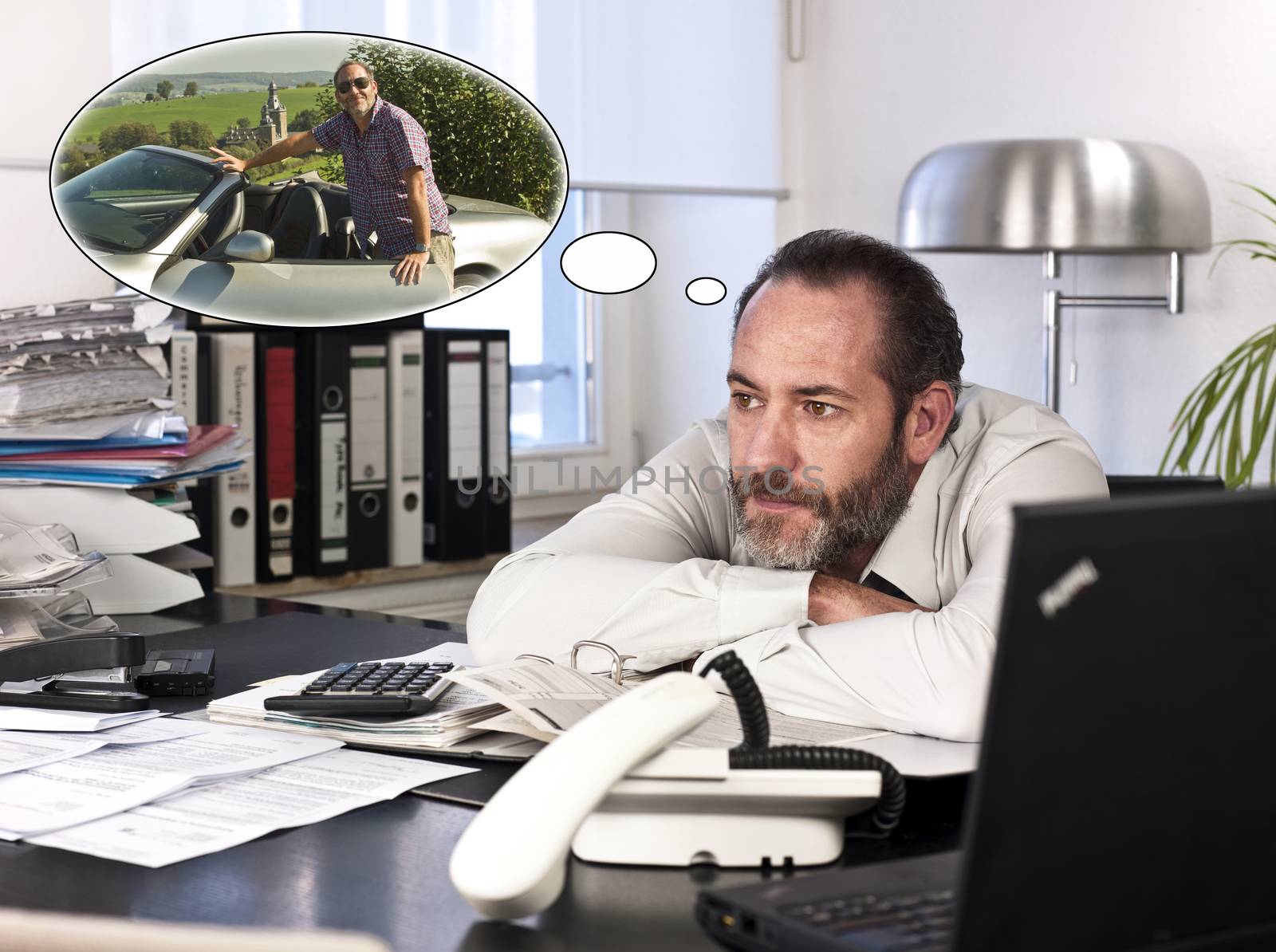 Mature businessman at desk with a thought bubble of himself and new car countryside. Horizontal shot