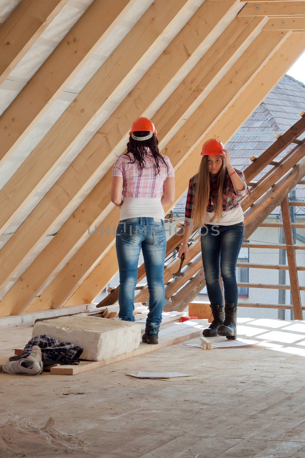 Two young long-haired woman hammered nails into a wooden construction of a new roof on the house