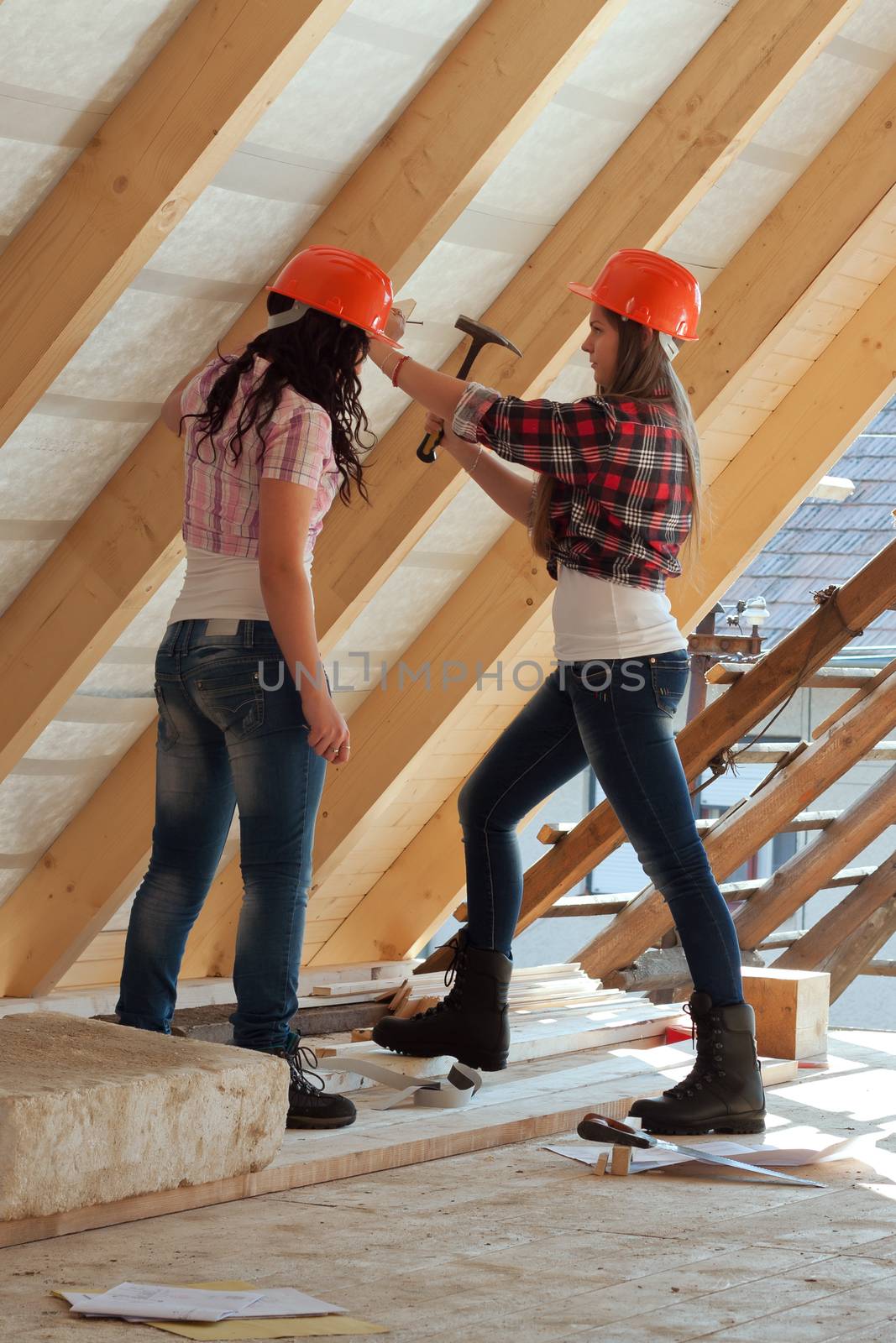 Two young long-haired woman hammered nails into a wooden construction of a new roof on the house