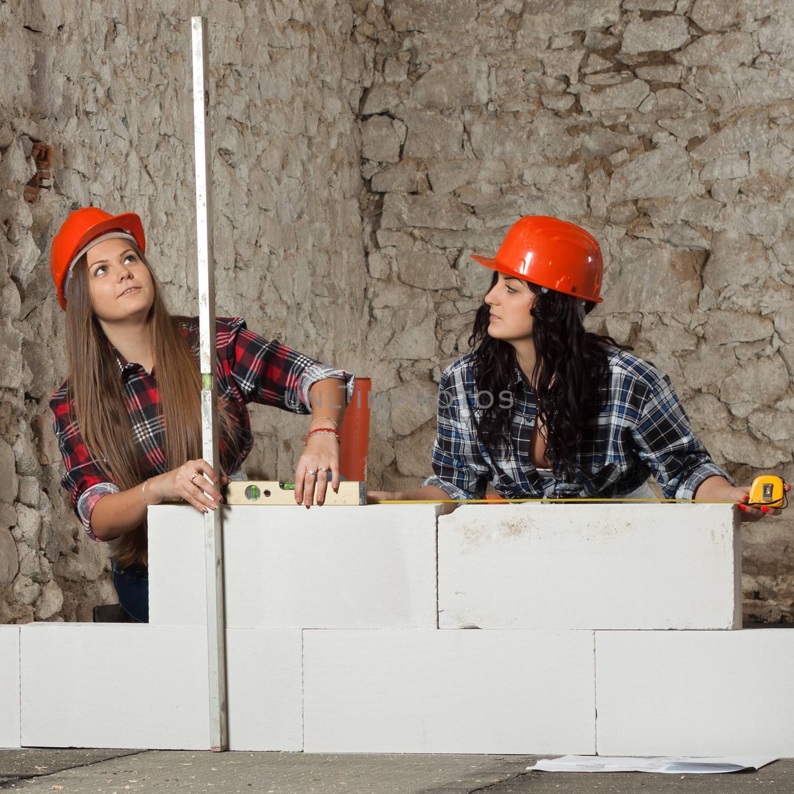 Two young long-haired woman repairing the old house and build a new wall from blocks in accordance with drawing