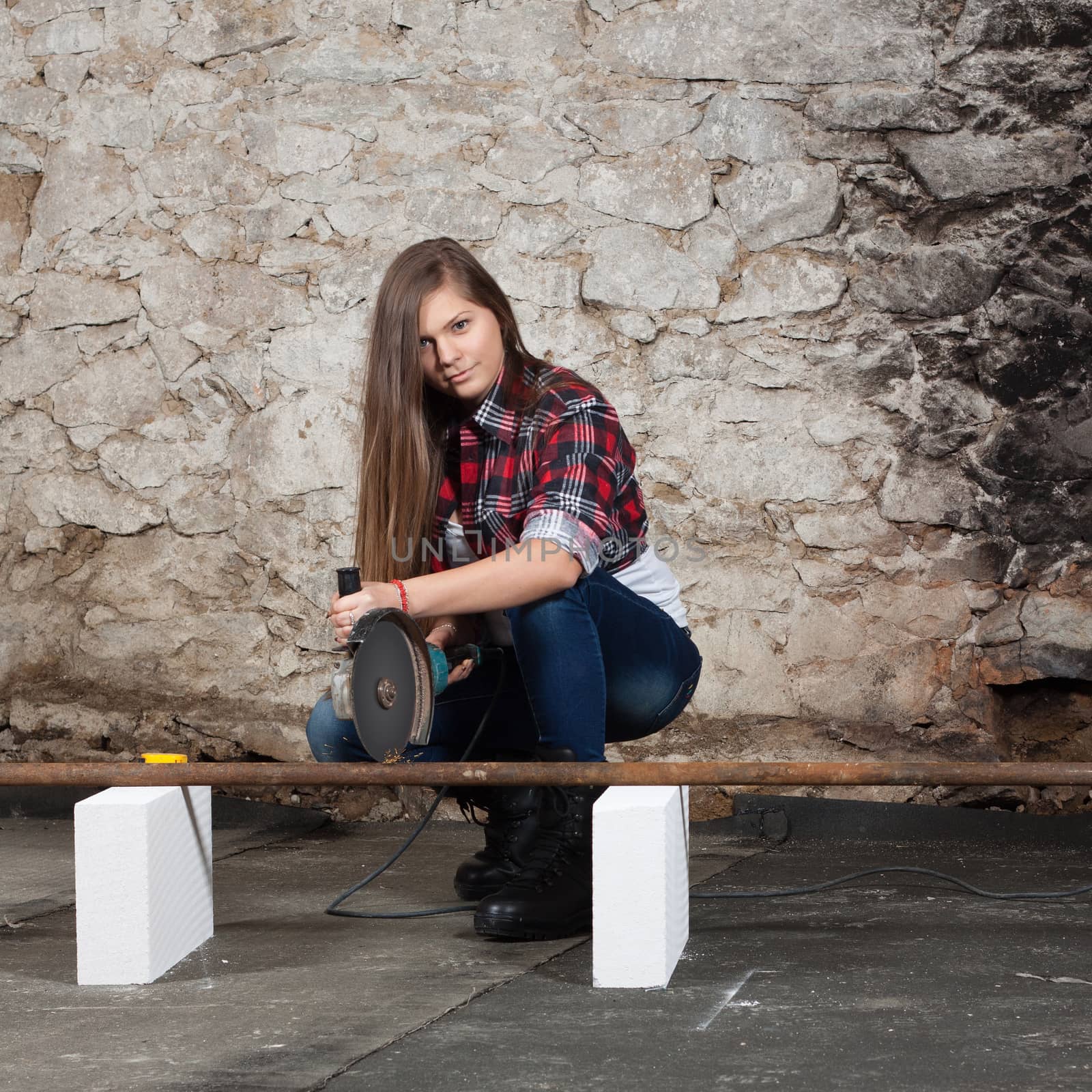 Young long-haired woman cut iron pipe with angle grinder during the repair an old house