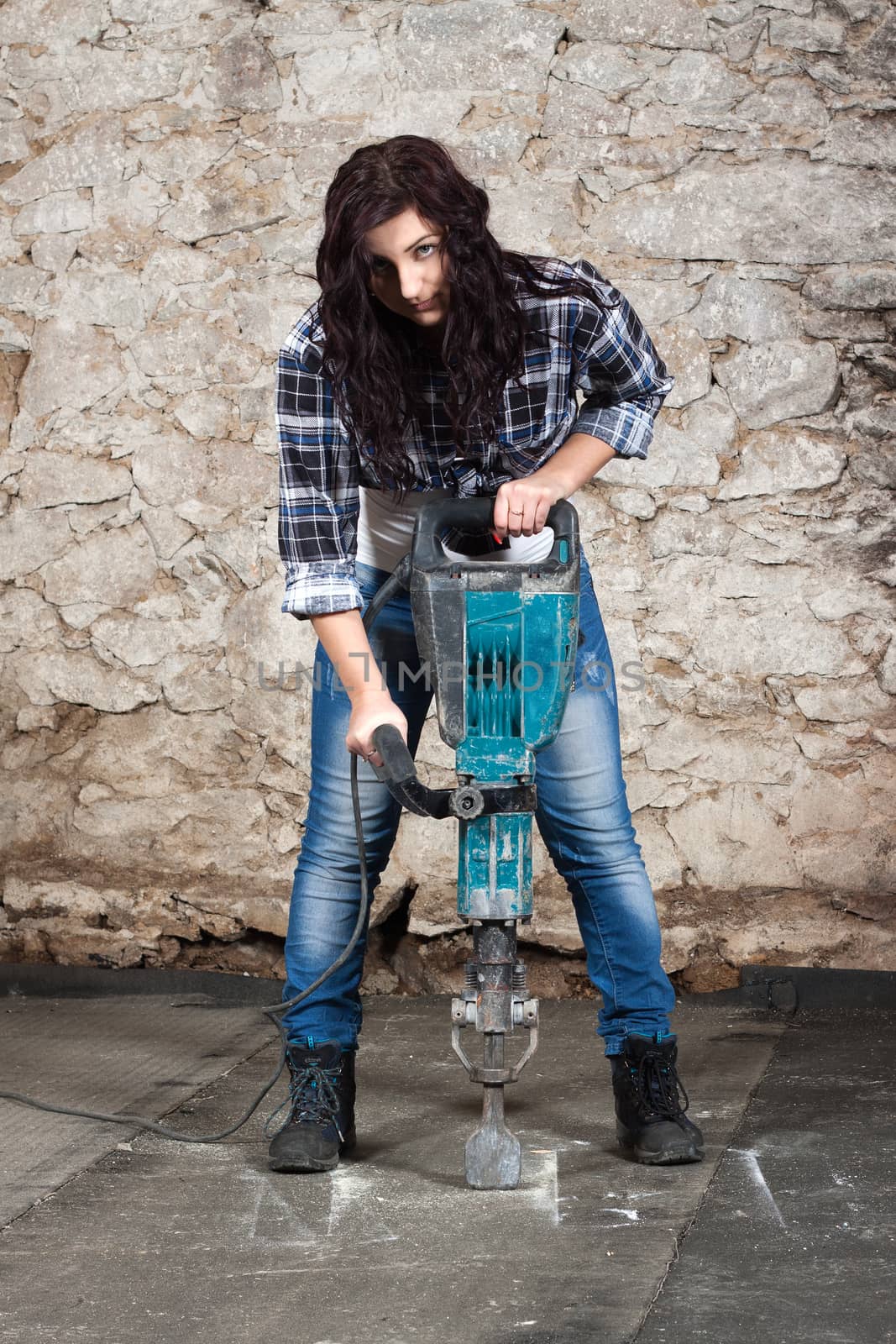 Young long-haired woman working with jackhammer during the repair an old house