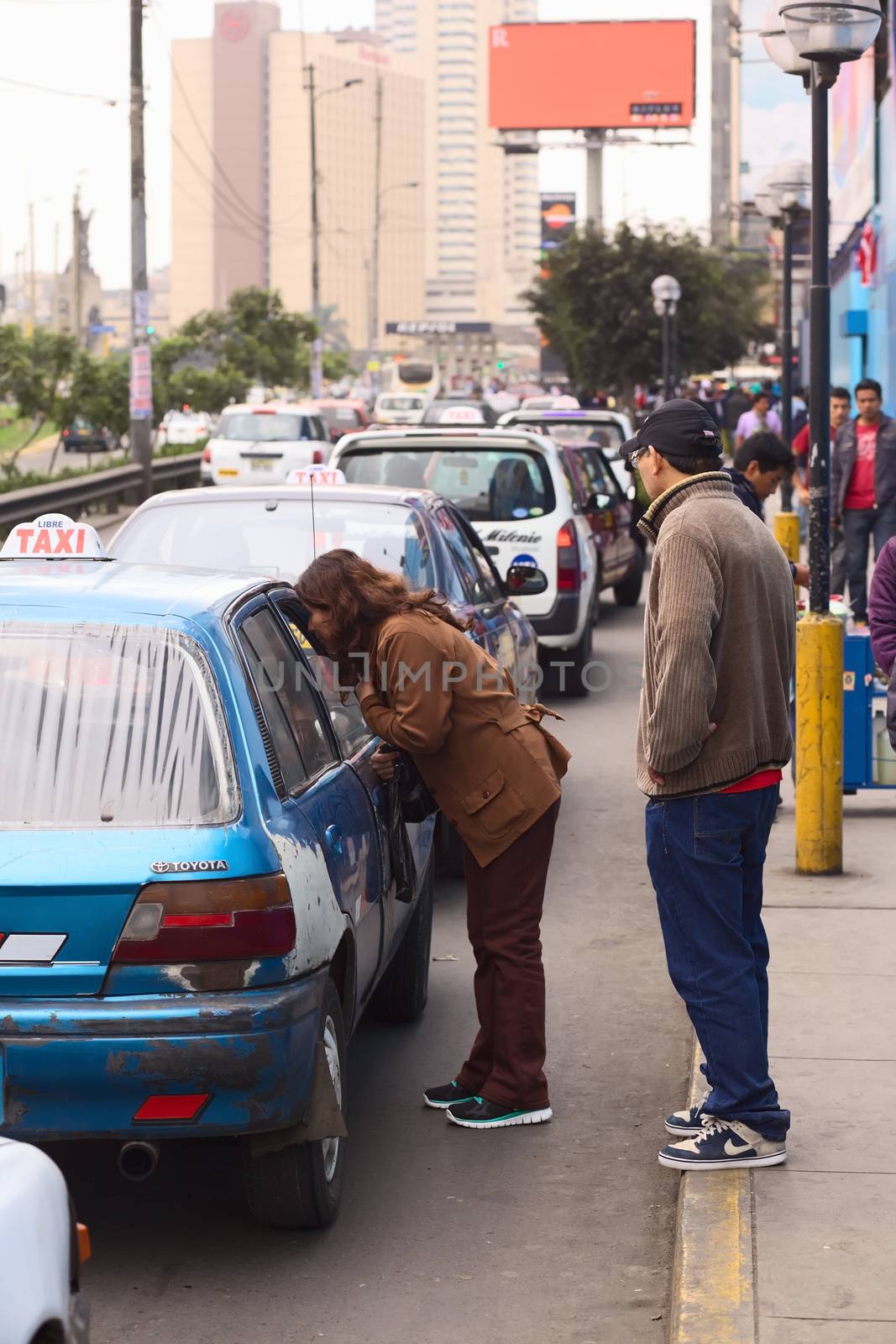 LIMA, PERU - JULY 21, 2013: Unidentified woman asking a taxi for the fare in front of the mall Polvos Azules on Av. Paseo de la Republica in the city center on July 21, 2013 in Lima, Peru. In Lima, taxi fares are agreed upon beforehand, fares are not standardized.