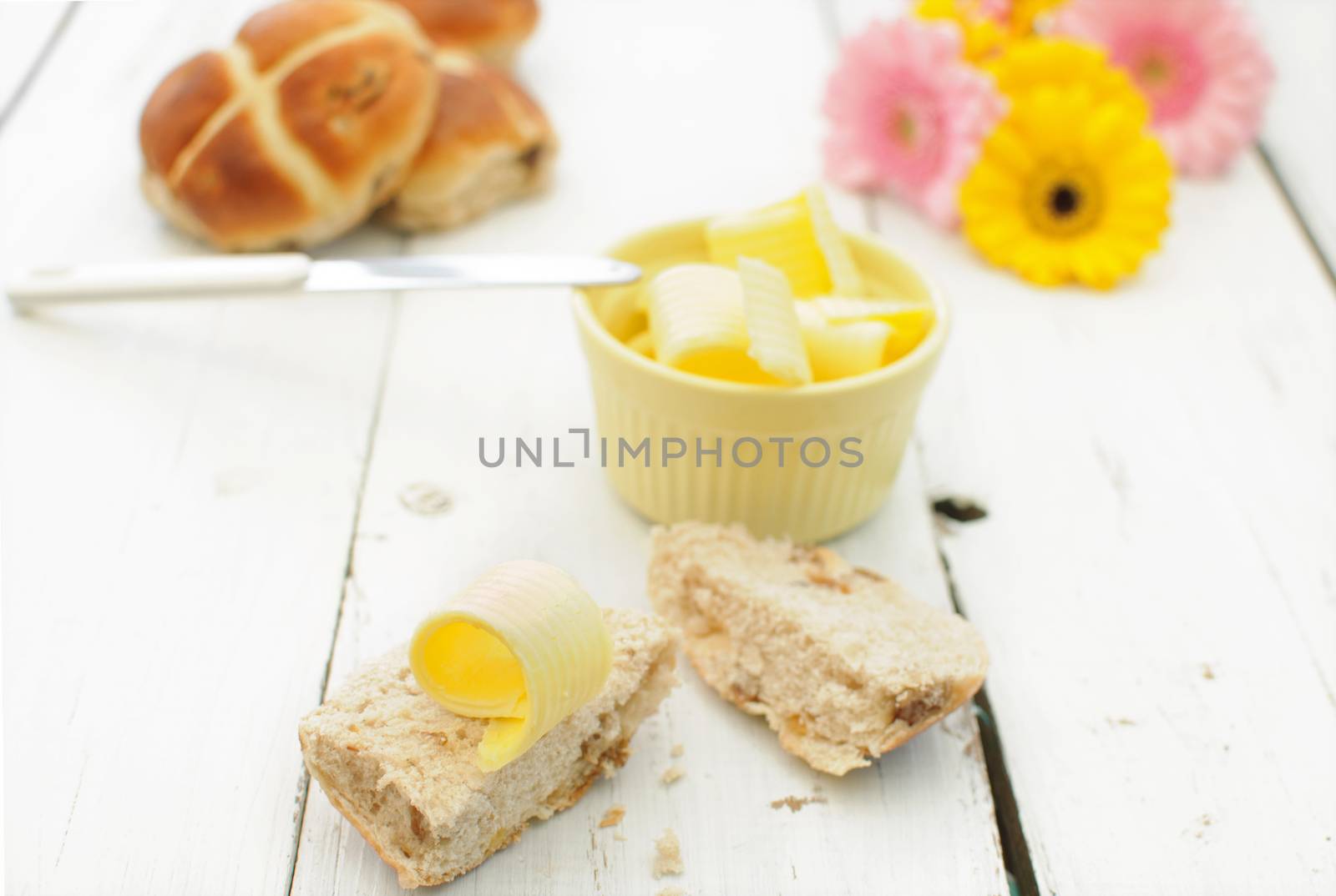 Hot cross bun cut into two with butter curls on the side 