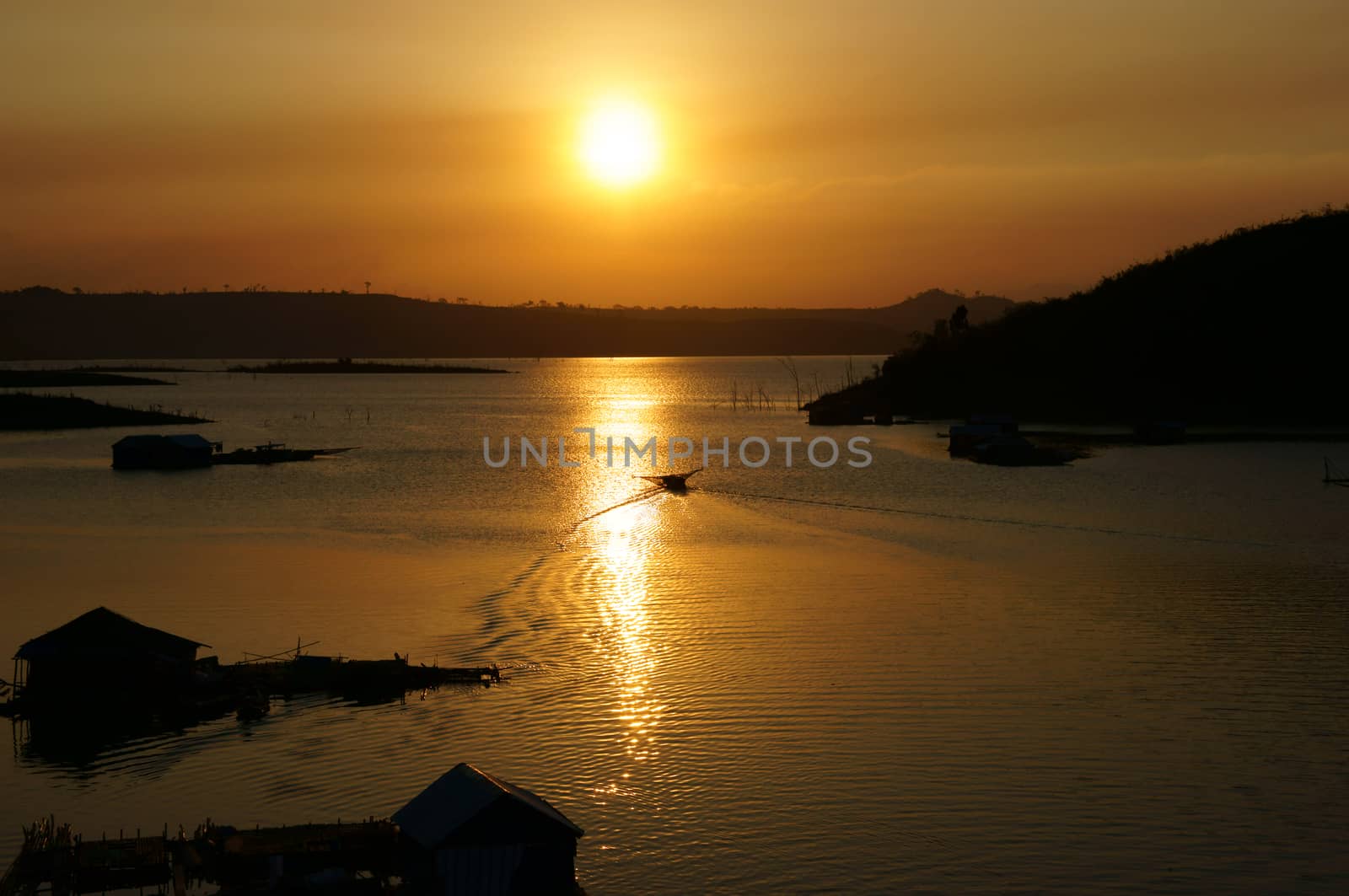 Sunset on fishing village, houses on water in silhouette, boat moving forward the su