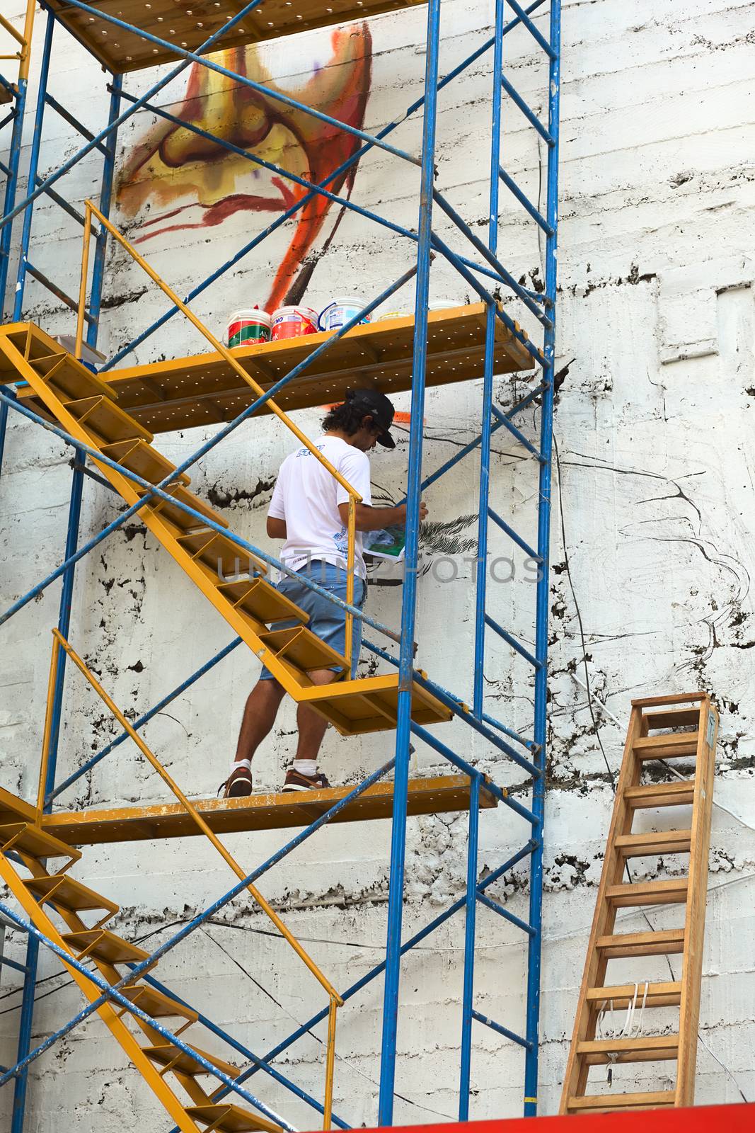 LIMA, PERU - MARCH 3, 2012: Unidentified young man painting a high outside wall of a building standing on a scaffold on March 3, 2012 in Miraflores, Lima, Peru